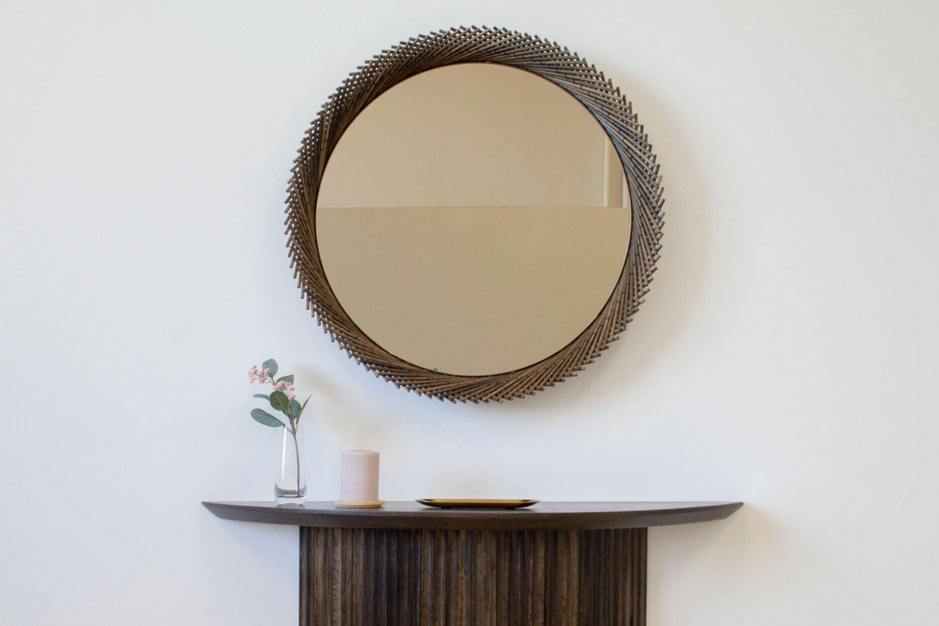 The Mooda Mirror is composed of a set of dowels stitched together to create a beautiful geometric edge around the glass. The mirror in turn reflects the dowels along its circumference, completing the traditional form of the Mooda.   Available in two