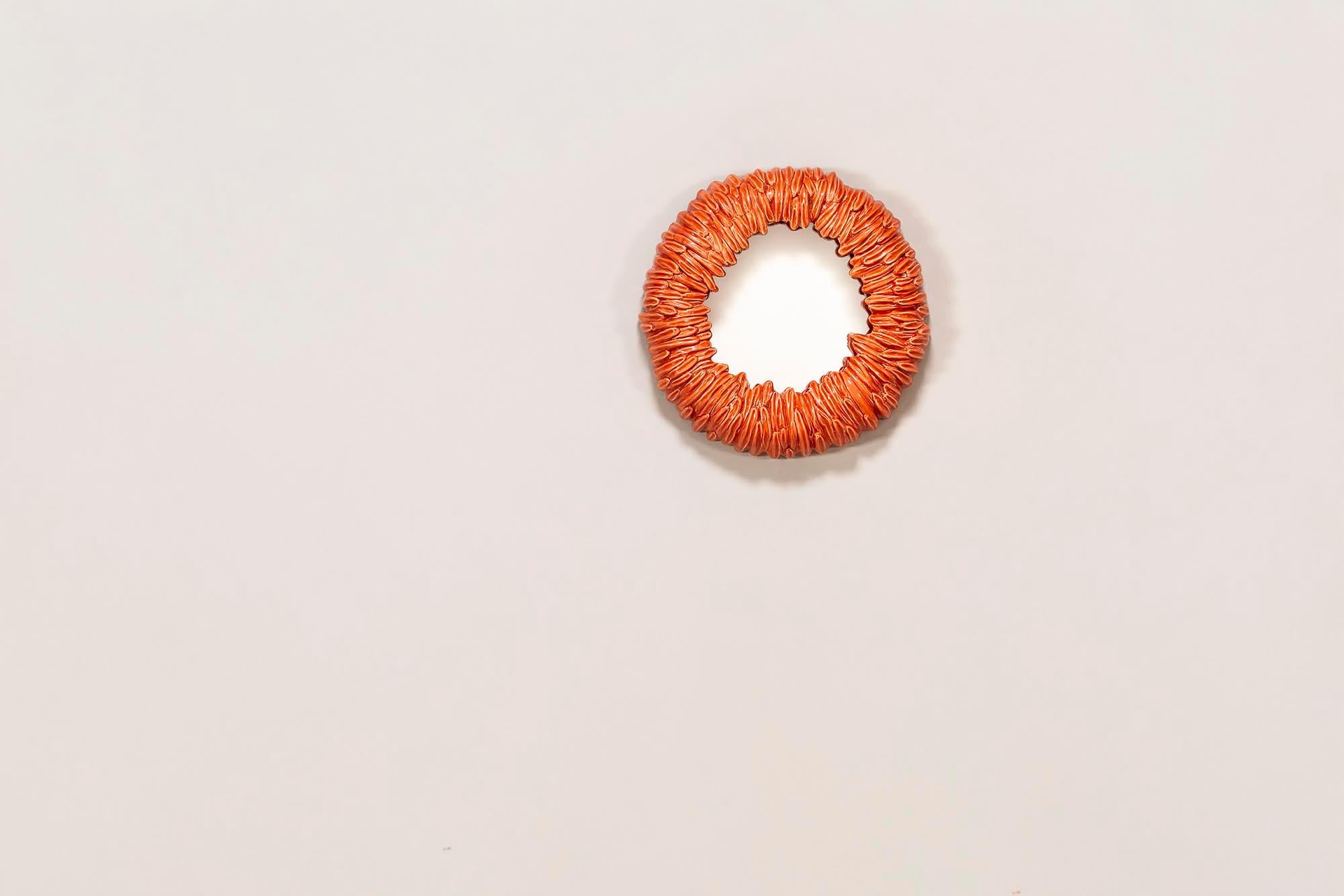 Ce miroir italien est une pièce qui attire le regard et qui allie savoir-faire artisanal et design audacieux. Le cadre, sculpté en céramique, a une teinte rouge-orange profonde qui dégage de la chaleur. Sa forme à la fois moderne et organique en