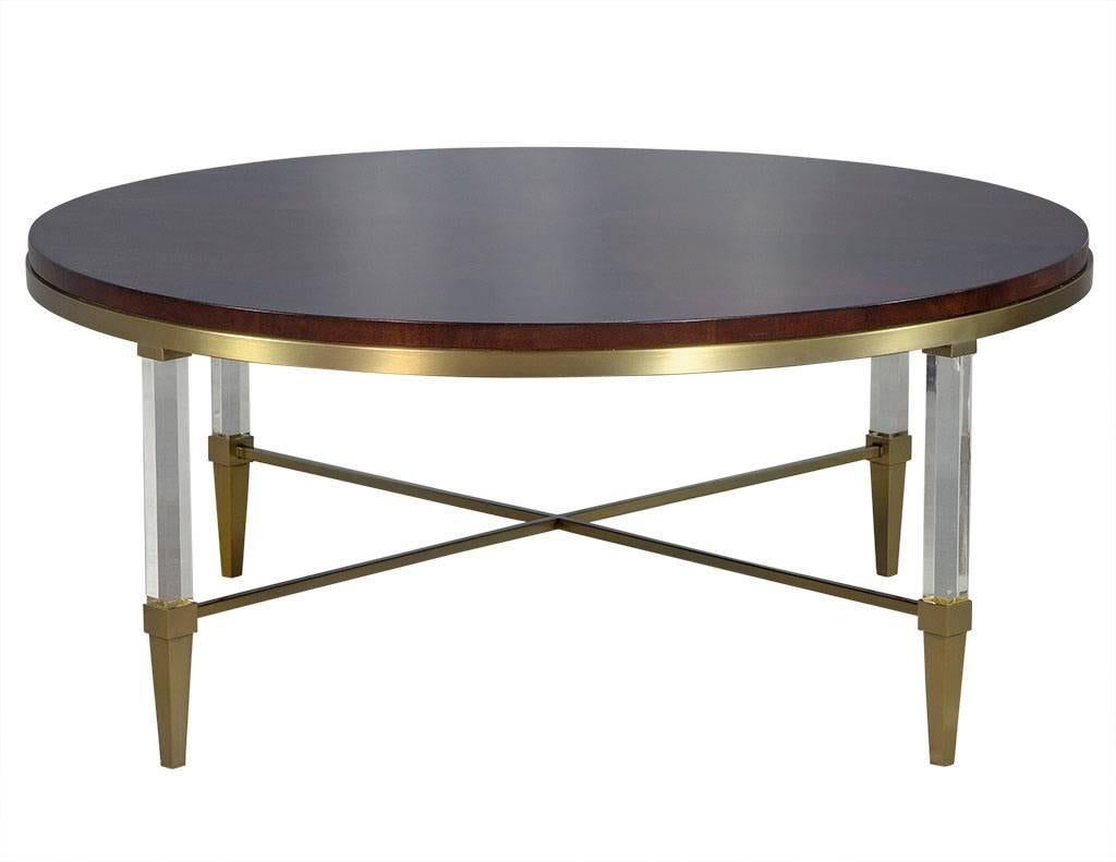 This modern coffee table has Asian flair.  Composed of a round wood top with brushed brass metal underneath, it sits atop lucite legs with tapered brass feet connected by x-shaped brass rods.  Perfect for a worldly living room!