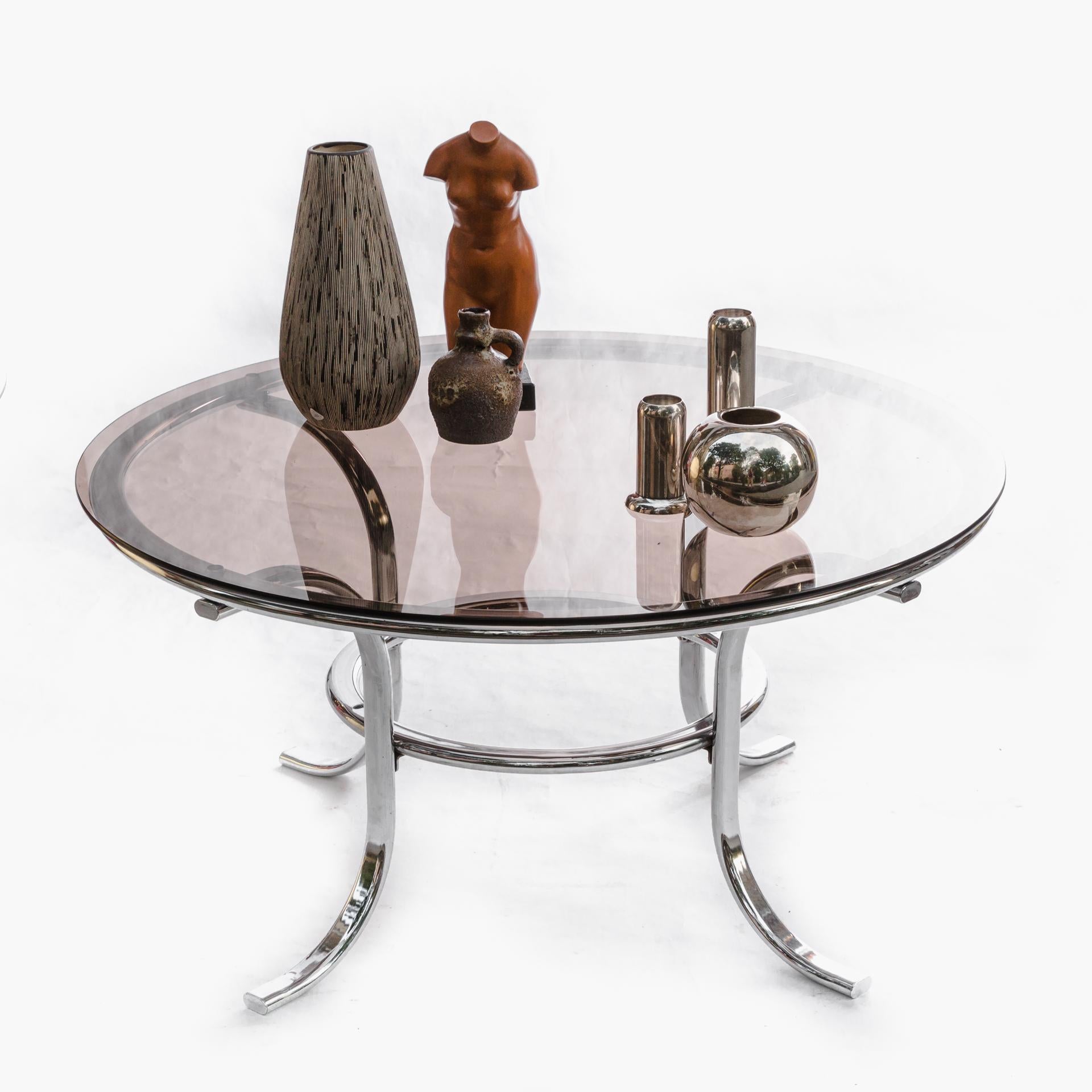 Round coffee table from the 1970s.

The table structure is made of bent chrome tubes. Round smoke glass top.

The furniture is an example of modernist design.
