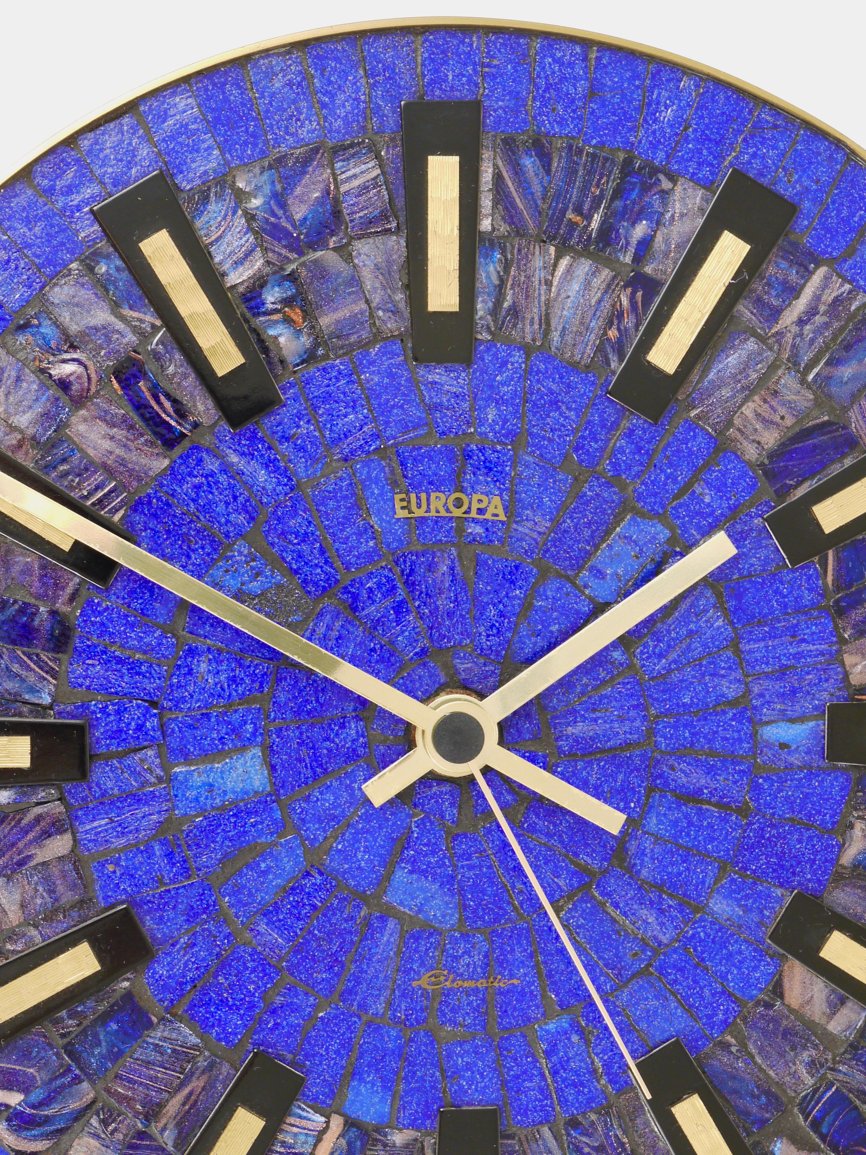 A beautiful round mid-century wall clock, with a brass frame, nice brass hands and indices and a stylish blue mosaic clocks´face. Executed in the 1950s by Europa, Germany. Original standard battery-operated movement. In very good condition. Fully