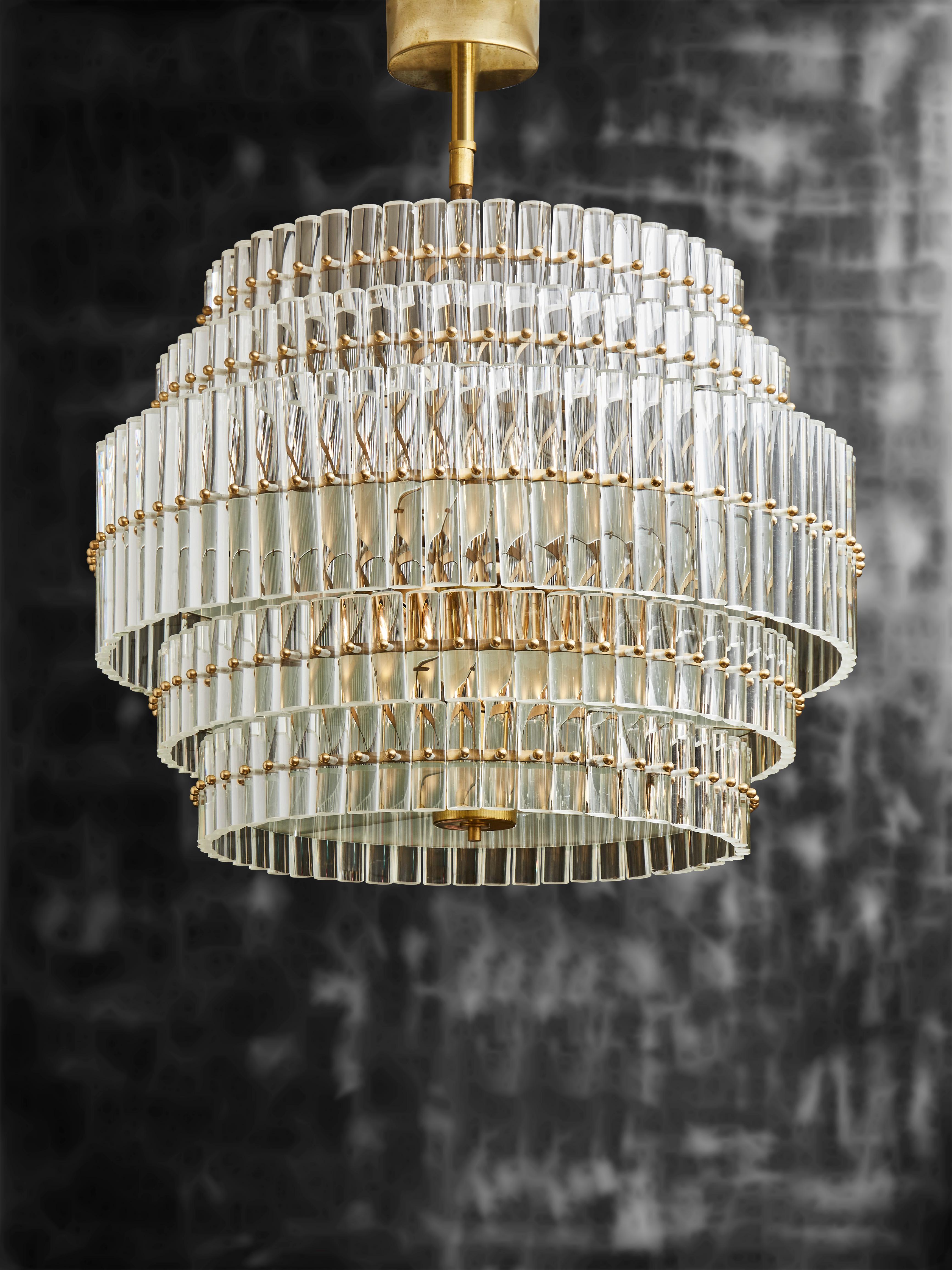 Circular chandelier made of several layers of rounded glass rods individually screwed to the structure.

Each floor has a different diameter adding volume to the piece, while the frosted glass sheets between the layers help spread the light and