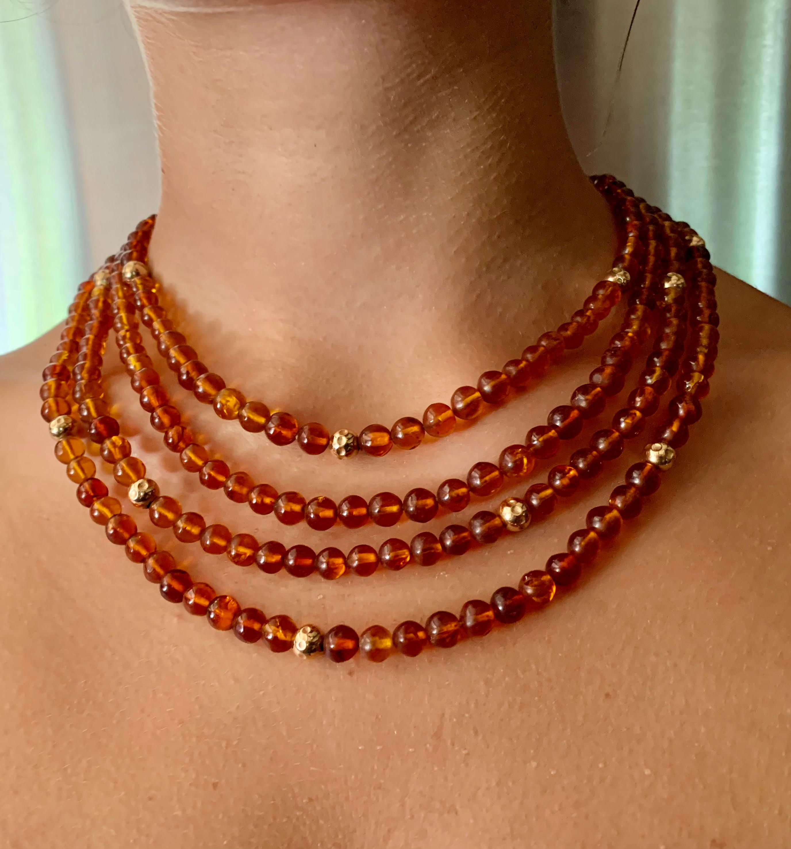 Early 20th Century round natural honey colored 5-6mm amber and hammered 5mm gold bead necklace composed of four strands. 
The amber beads lively, ranging in color from a golden yellow to light orange honey color with natural inclusions, slightly