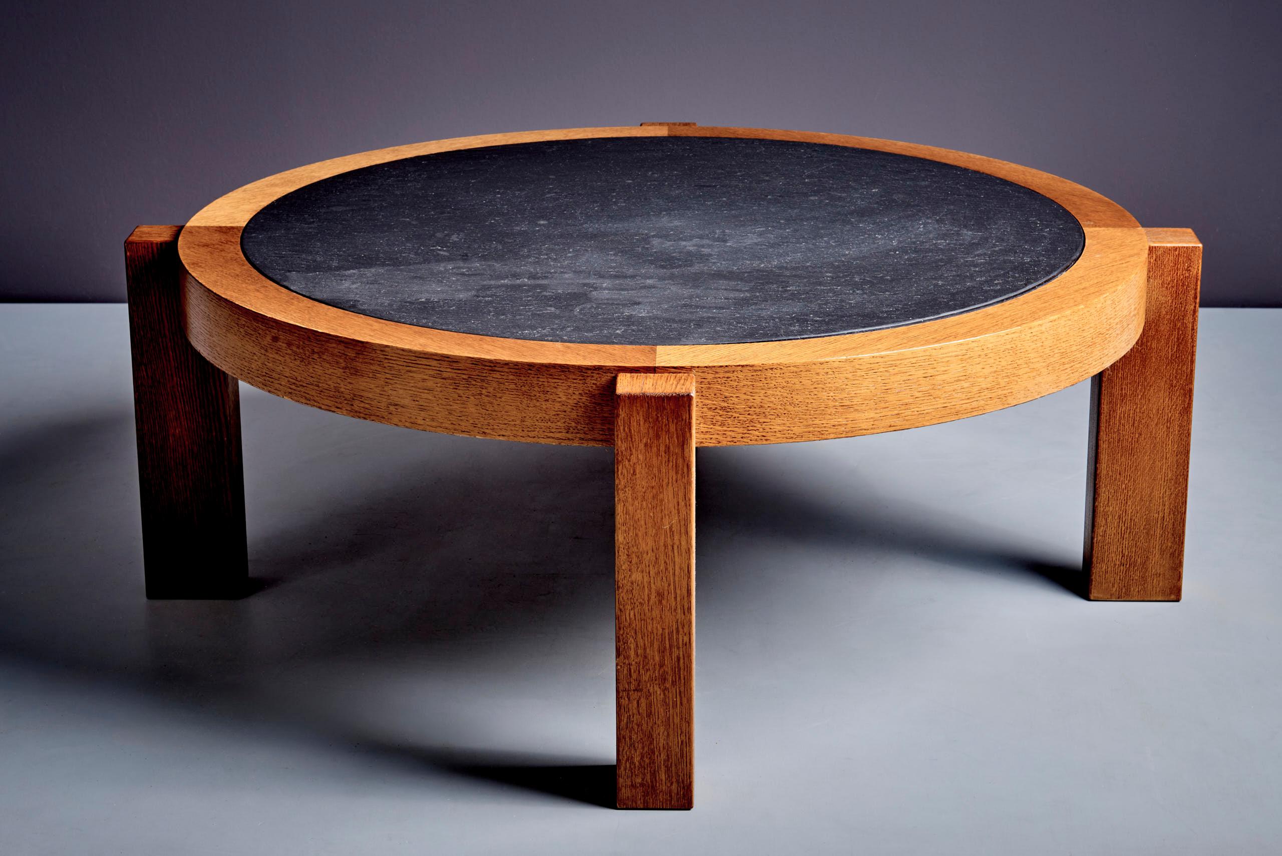 Table basse ronde avec plateau en pierre d'ardoise foncée et structure en chêne. La pierre présente une surface texturée naturelle, qui contraste avec la chaleur du bois de chêne. La table repose sur quatre solides pieds carrés fixés dans le cadre