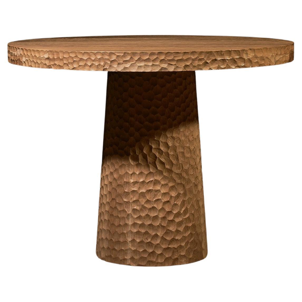 Cette table de salle à manger ronde est fabriquée en chêne massif et finie avec un léger badigeon qui révèle délicatement le grain naturel du bois. La base conique donne à la pièce une impression de stabilité tout en conservant une présence légère