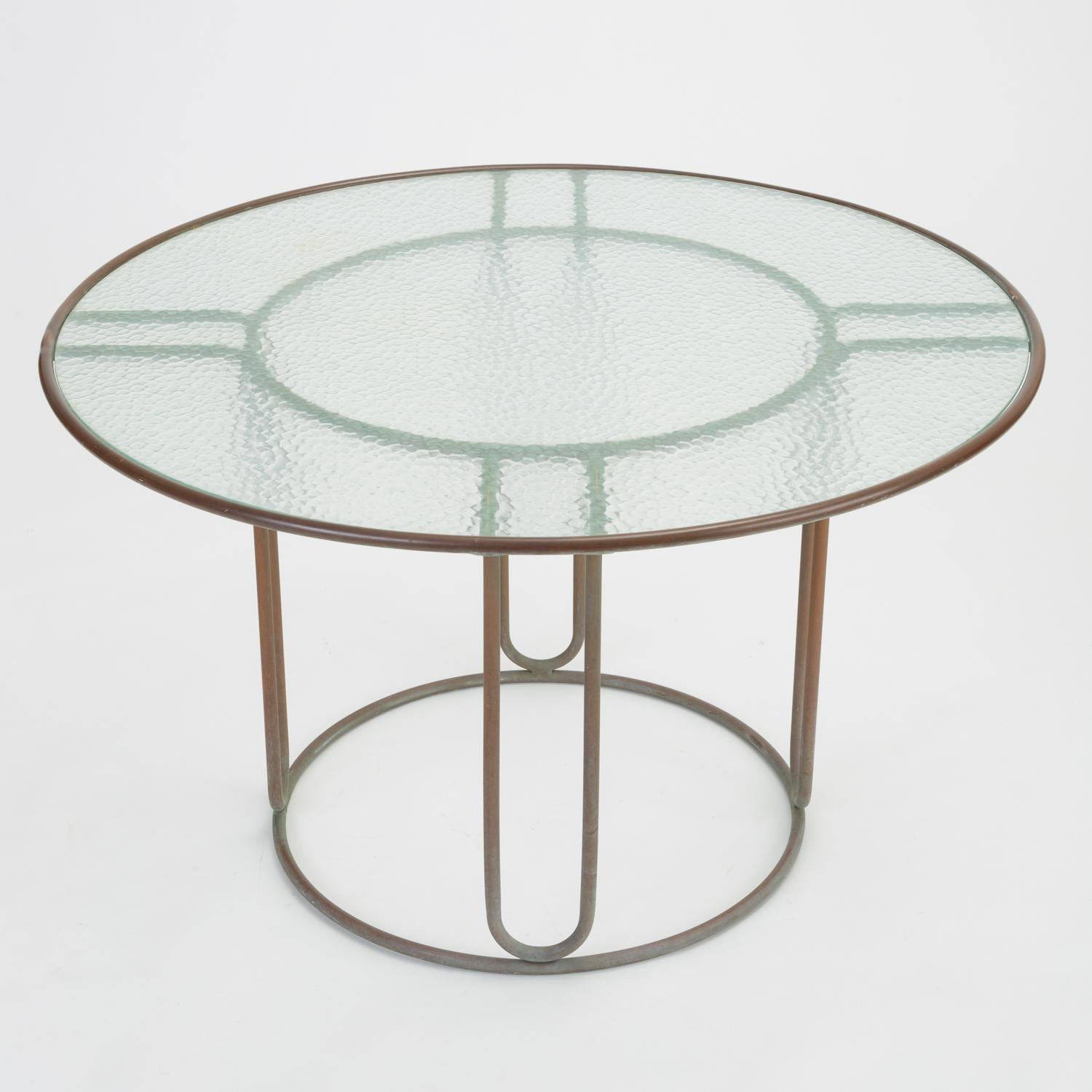 A patio dining table in patinated bronze designed by Walter Lamb and produced by Brown Jordan. The round frame is described by two concentric rings of bronze with radial supports and a circular bronze base. The round tabletop is a single piece of