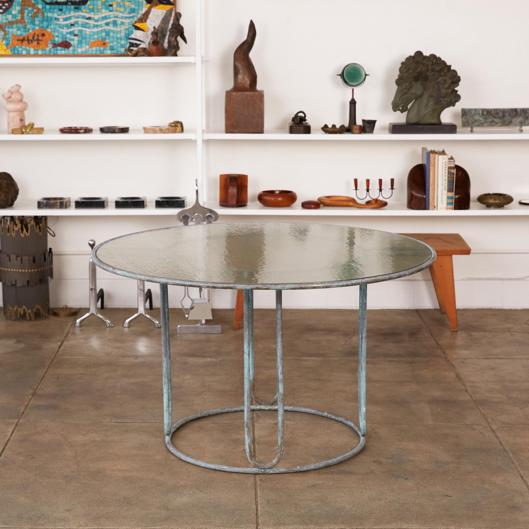 A patio dining table in patinated bronze designed by Walter Lamb and produced by Brown Jordan. The round frame is described by two concentric rings of bronze with radial supports and a circular bronze base. The round tabletop is a single piece of