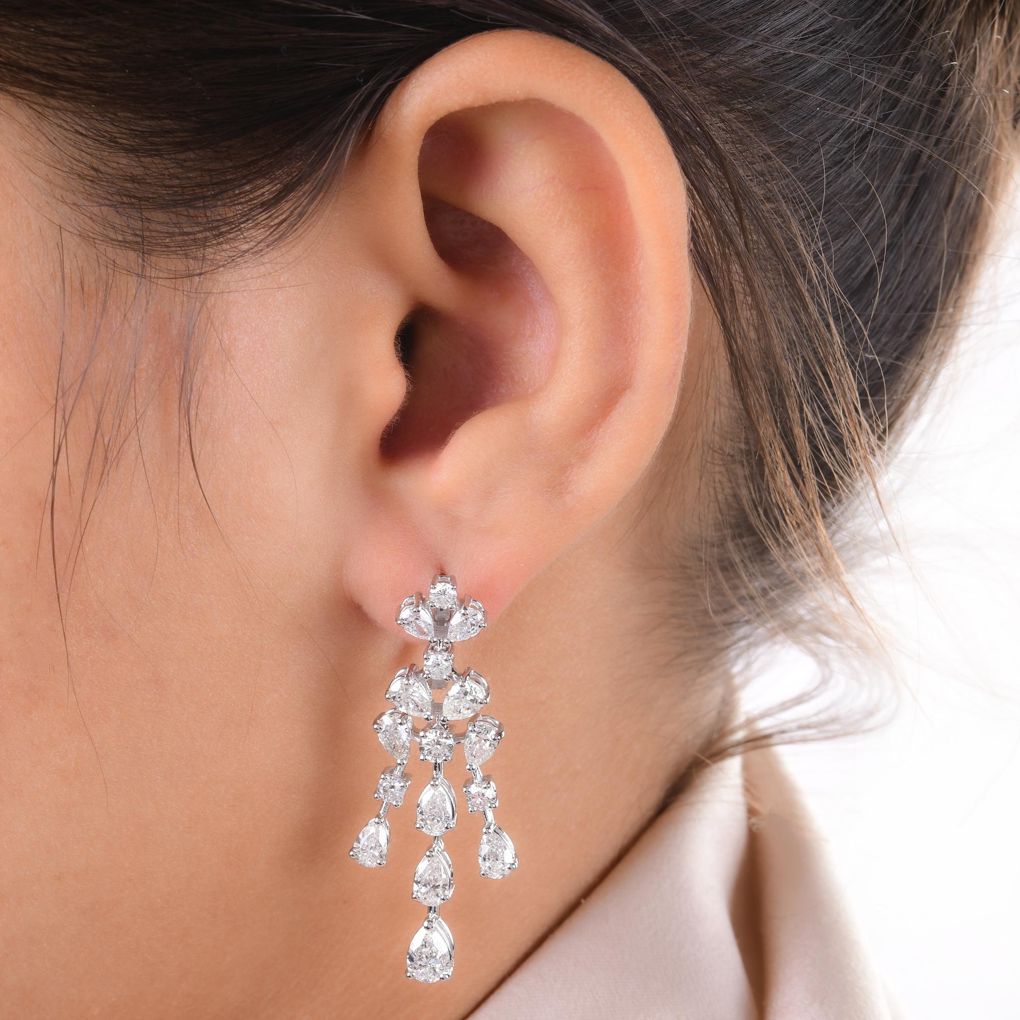 At the center of each earring, a dazzling Round Diamond takes center stage, showcasing its brilliance and fire with every movement. Surrounding the round diamond are delicate Pear Shape Diamonds, adding a touch of allure and uniqueness to the