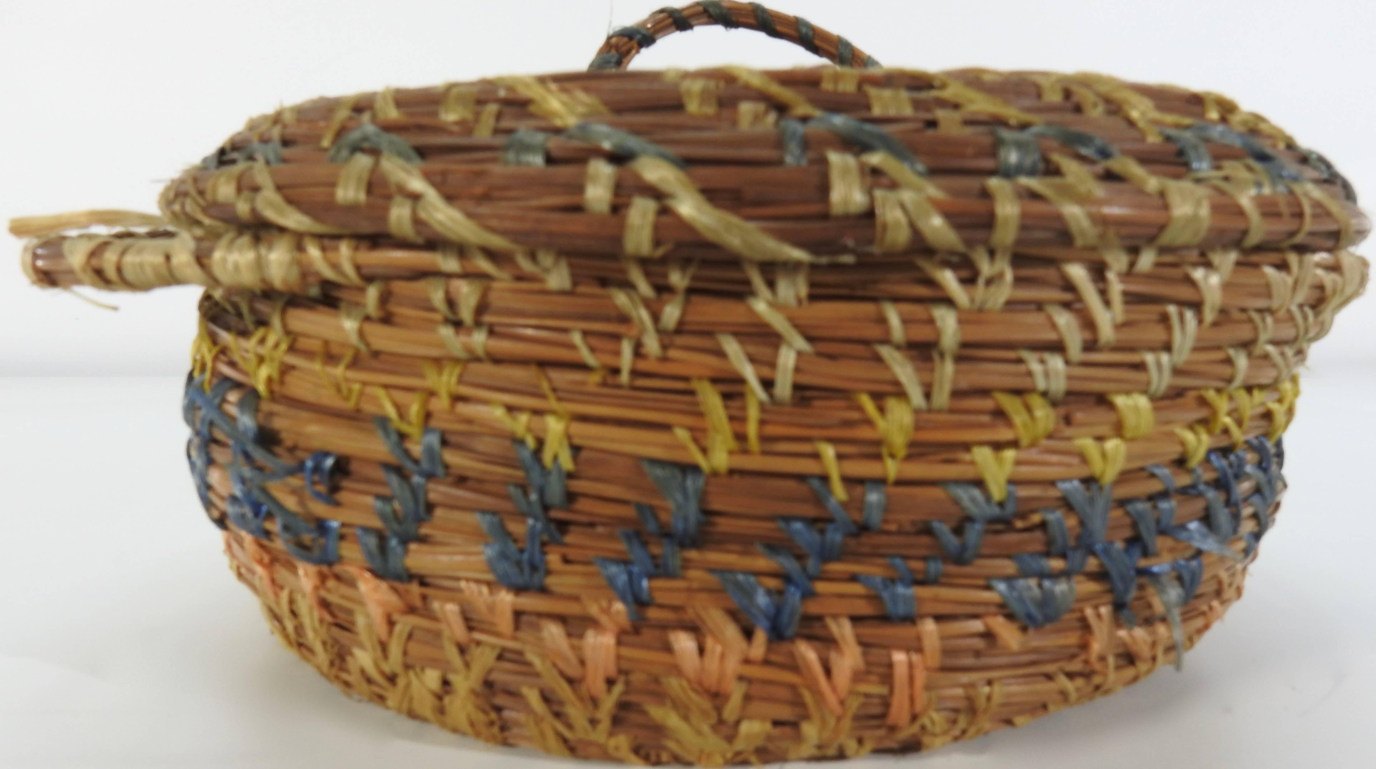 This vintage basket from 1940s is constructed of pine straw and accented with various shades of dyed raffia. There is a handle for removing the lid and two handles on the base.