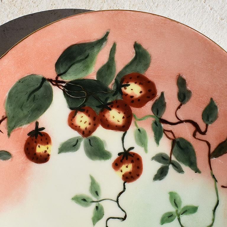 A beautiful ceramic saucer, catchall, or decorative trinket dish. Created from ceramic, this pretty plate is painted from crisp white ceramic or porcelain, and decorated with a pink strawberry motif on the front. The rim is painted with gold detail