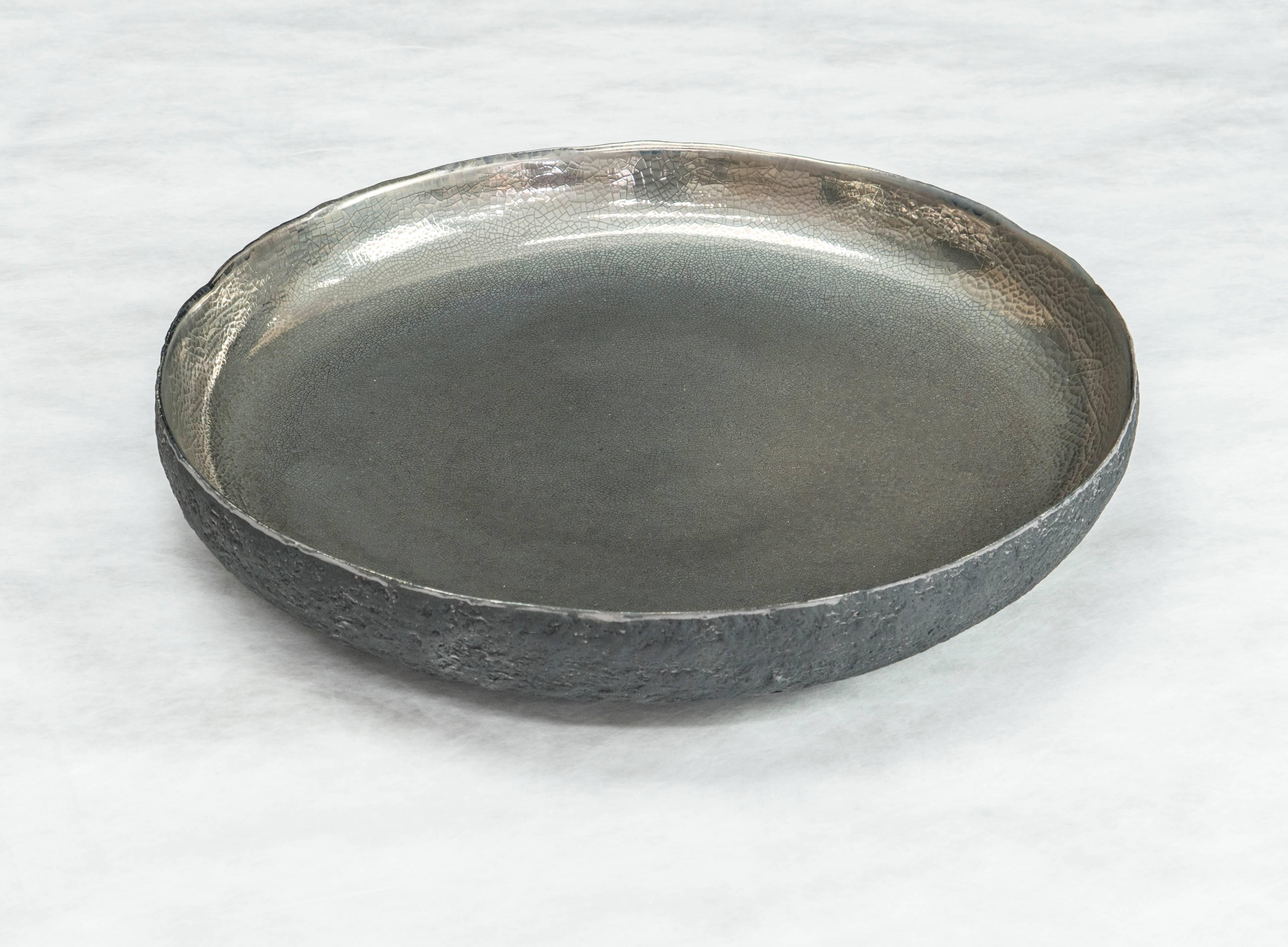 Beginning with a ball of clay, Cristina Salusti pinches it into vessels and textures them with stone fragments. 

After multiple firing it is finally lustered with platinum. 

Its volcanic-like outer wall seems protective of its precious gold center
