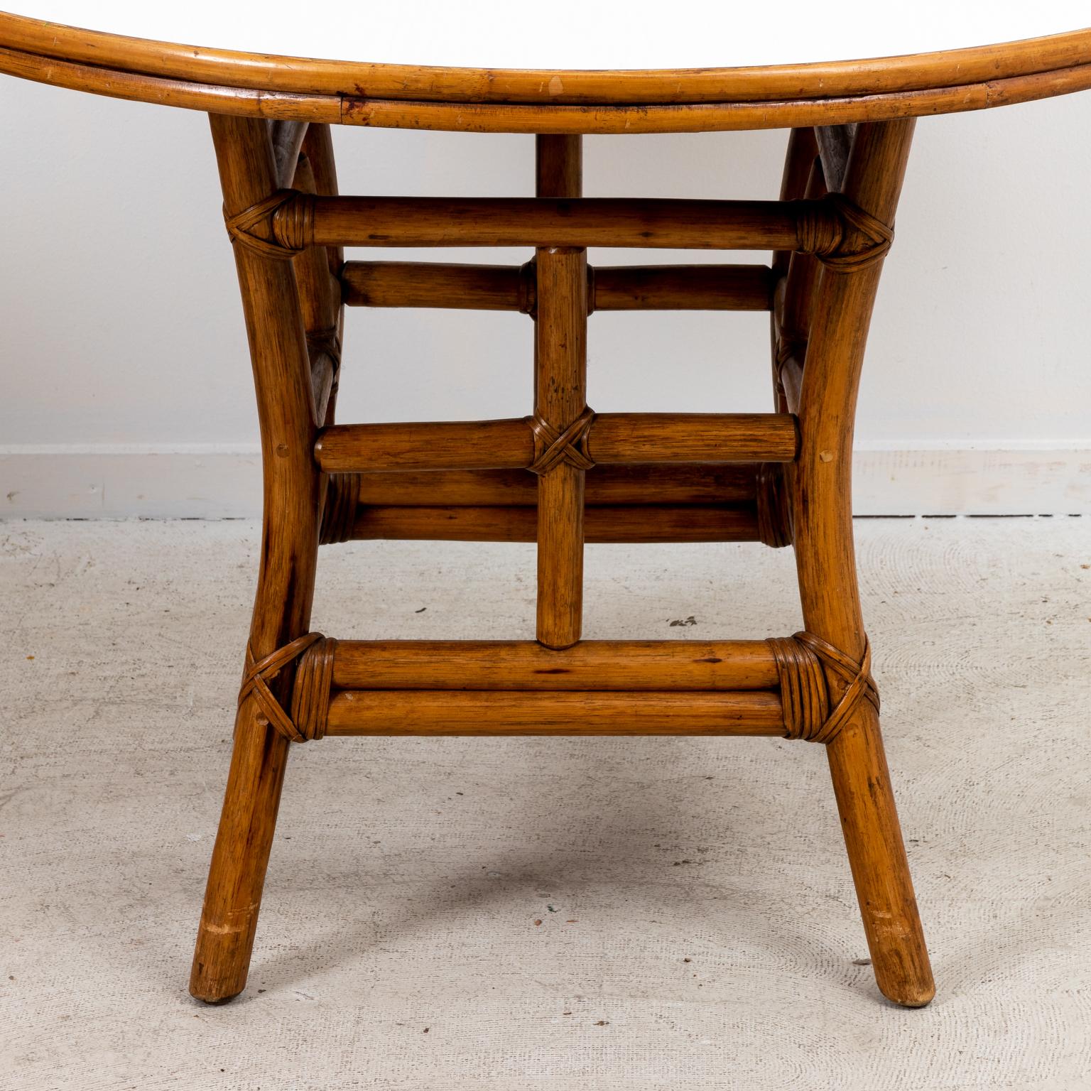 Circa 1970s Mid-Century Modern style round rattan dining table with oak grained white Formica top and rattan base. The piece measures 42.00 Inches diameter.