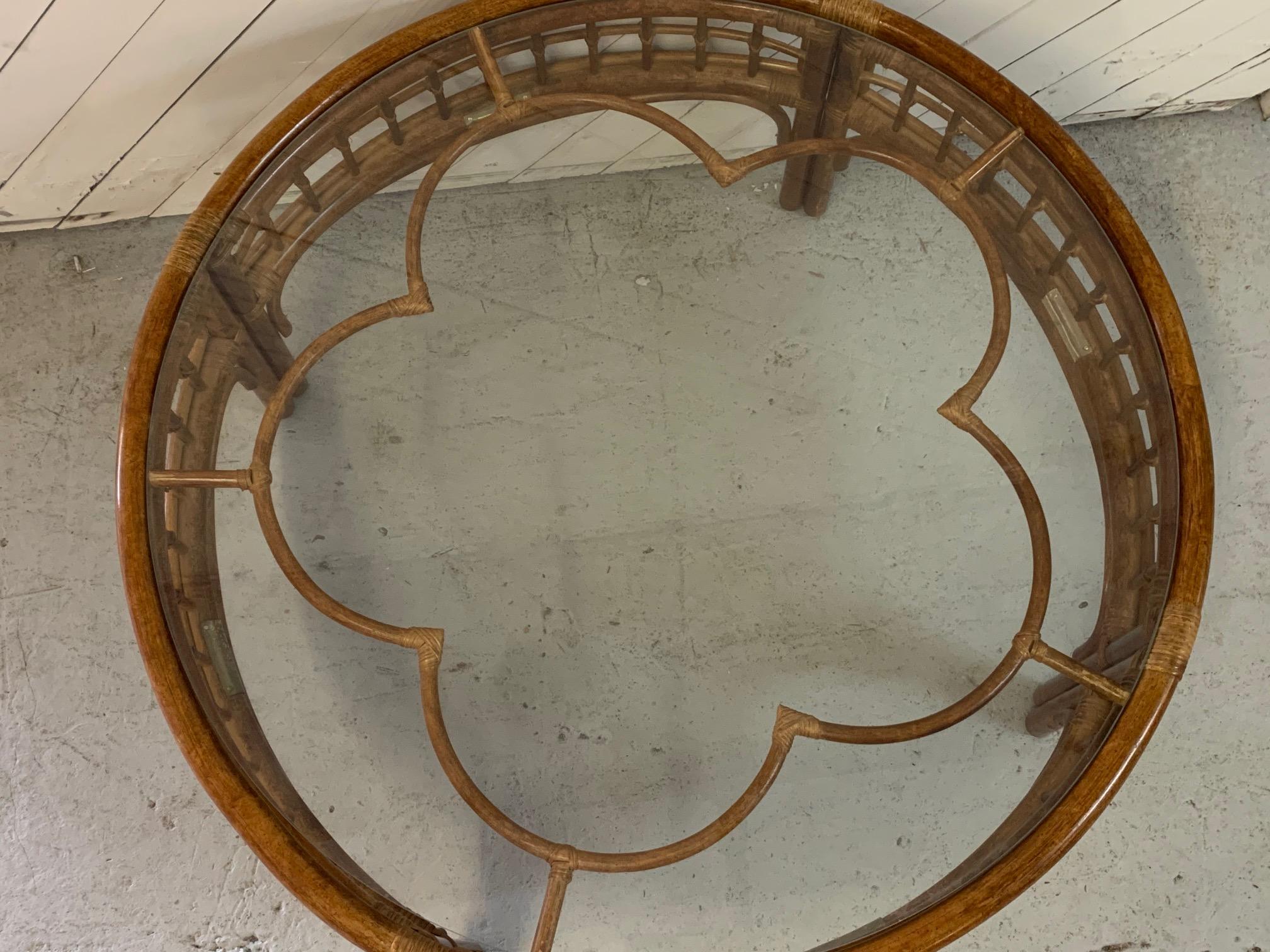 Midcentury rattan coffee/cocktail table features round design and brass accents. Glass top with rattan flower shape detailing. Very good vintage condition with minor imperfections consistent with age.