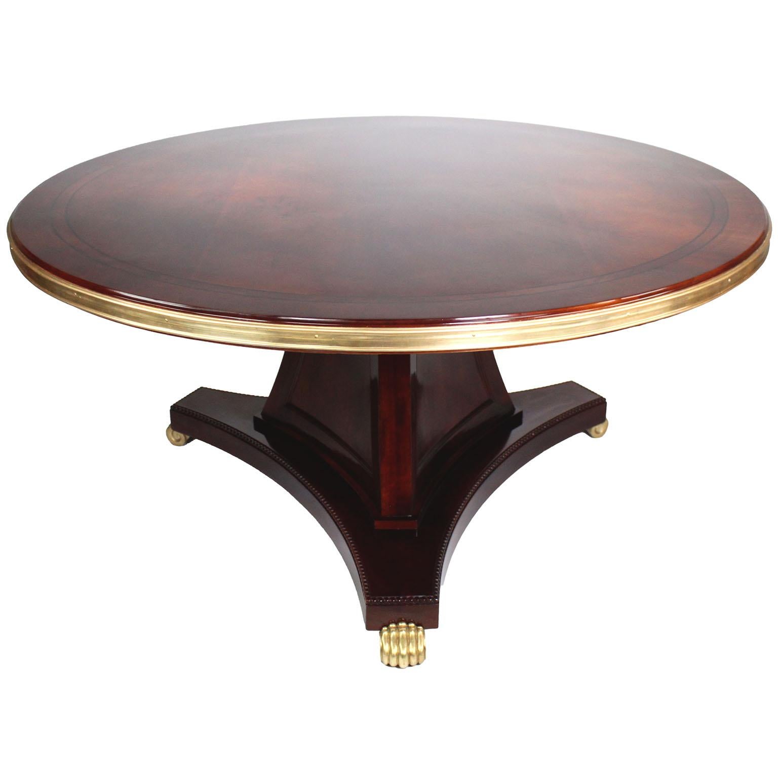 A Fine English Regency Style Mahogany and Gilt-Bronze Mounted Round Center Table or Game Table, Attributed to Maple & Co. The large circular mahogany veneered top, with twin ebonized inlaid border design, a gilt-bronze banded apron and raise on a