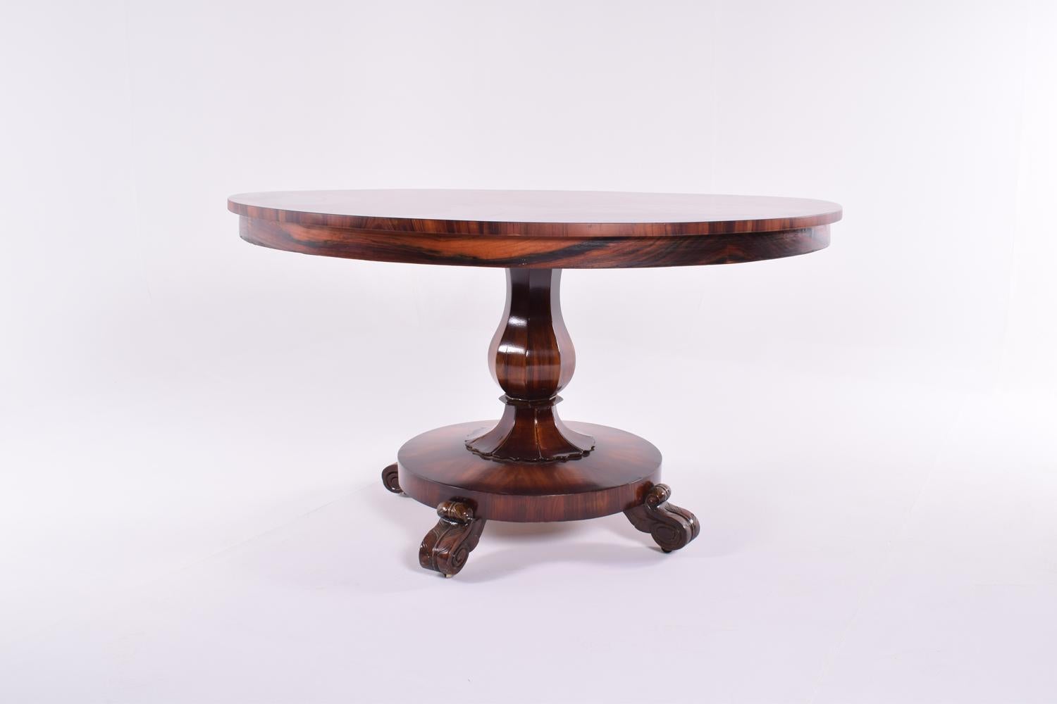 This circular rosewood breakfast/center table is veneered in some finely figured Rosewood veneers. The radially veneered platform base, sits on four carved paw feet showing good definition. Supported on the facetted centre stem, the tilt-top are