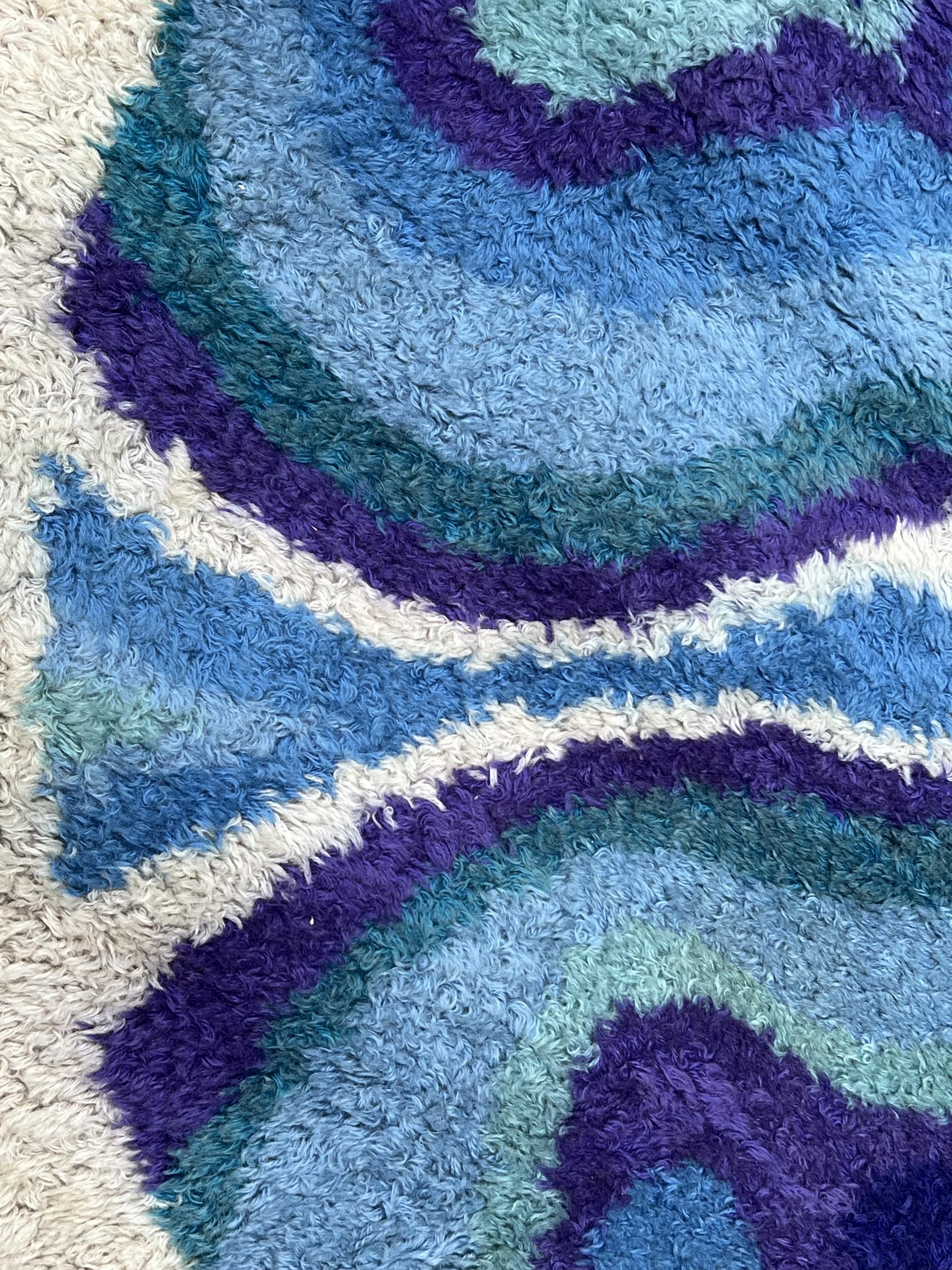 Interesting round rug in curly wool with « psychedelic » decoration, very typical of the 70s.
Dark blue, light blue, turquoise, dark green, water green and violet scrolls and arabesques on an off-white background.
