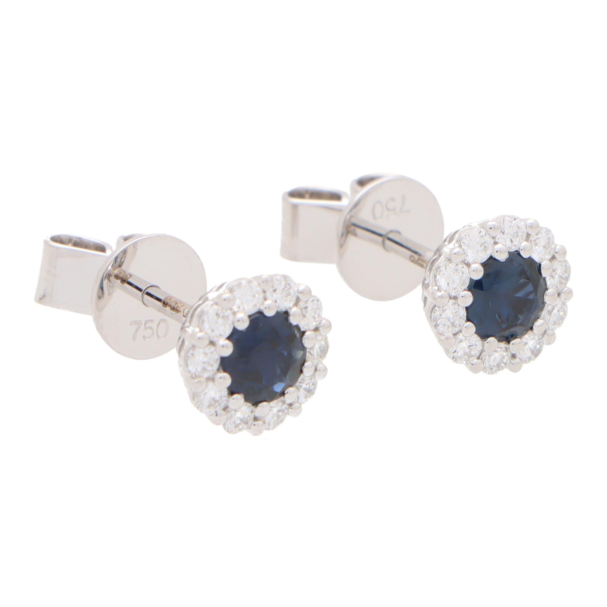 A beautiful pair of sapphire and diamond circular cluster earrings set in 18k white gold.

Each earring centrally features a beautiful royal blue coloured round cut sapphire surrounded by a halo of 10 round brilliant-cut diamonds. All of the stones