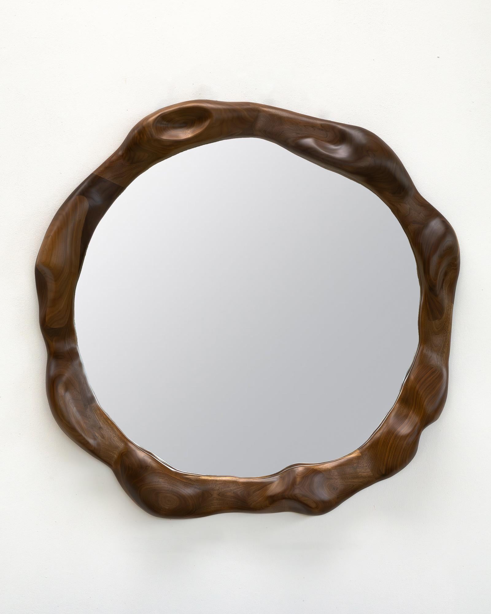 The frame of the mirror is shaped using various hand tools, making each piece unique with its own distinctive wood grain. It is made from high-quality walnut wood and finished with a hardwax oil. 

The mirror is mounted on the wall by hanging it on