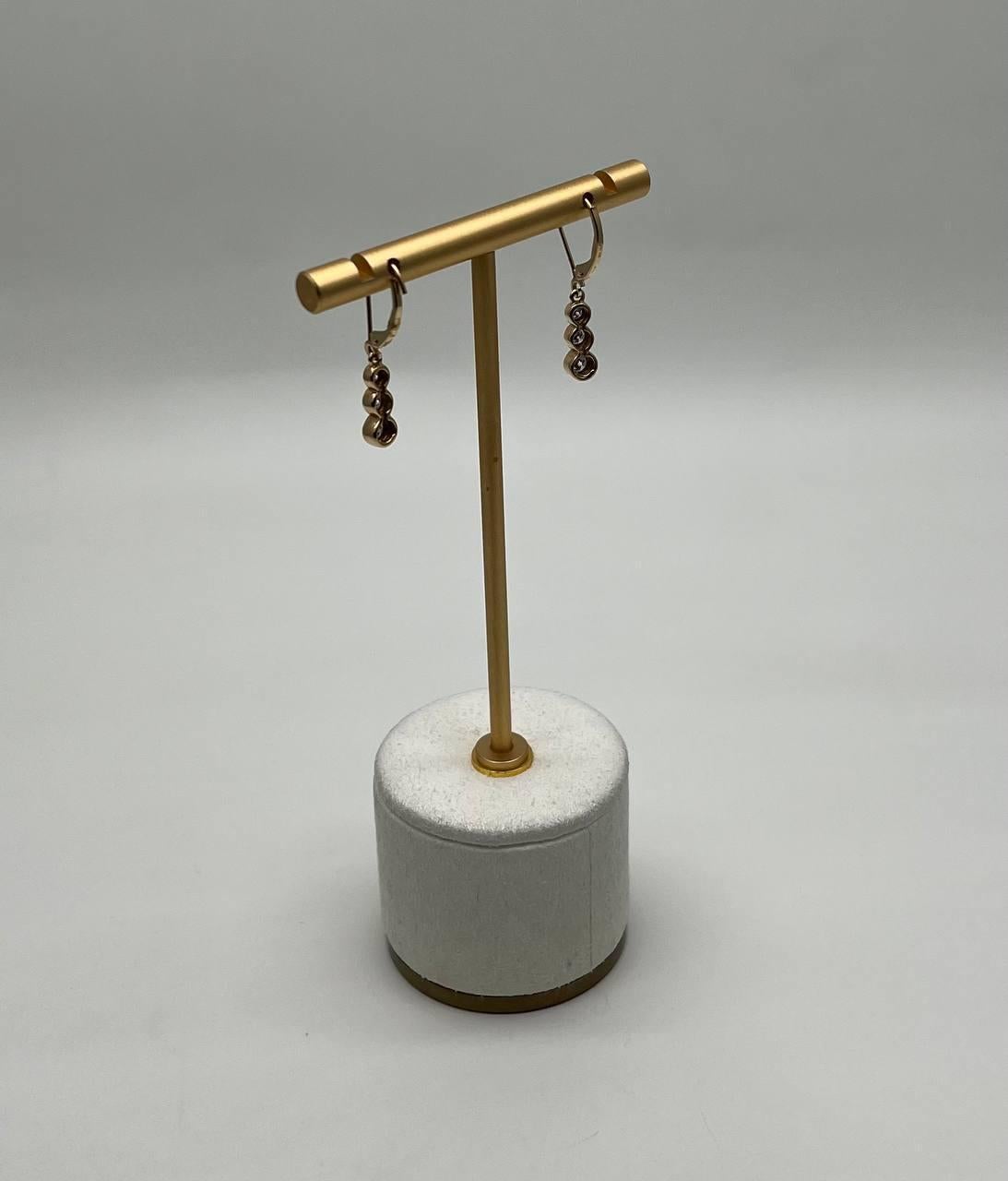 A refined pair of earrings, each crafted with precision, featuring a series of bezel-set round stones in a cascading design. The earrings are suspended from delicate hooks, offering a graceful movement. The gold finish enhances the brilliance of the
