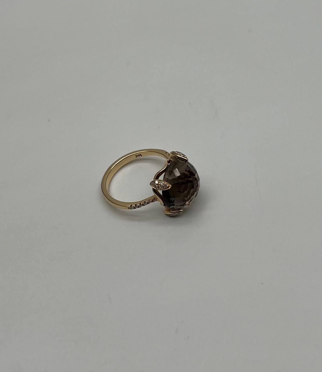 Scopri l'eleganza del nostro squisito anello. Questo affascinante pezzo presenta una gemma sfaccettata, simile a un quarzo fumé, incastonata in una raffinata fascia d'oro. La gemma è tenuta saldamente da quattro rebbi, ognuno dei quali è ornato da