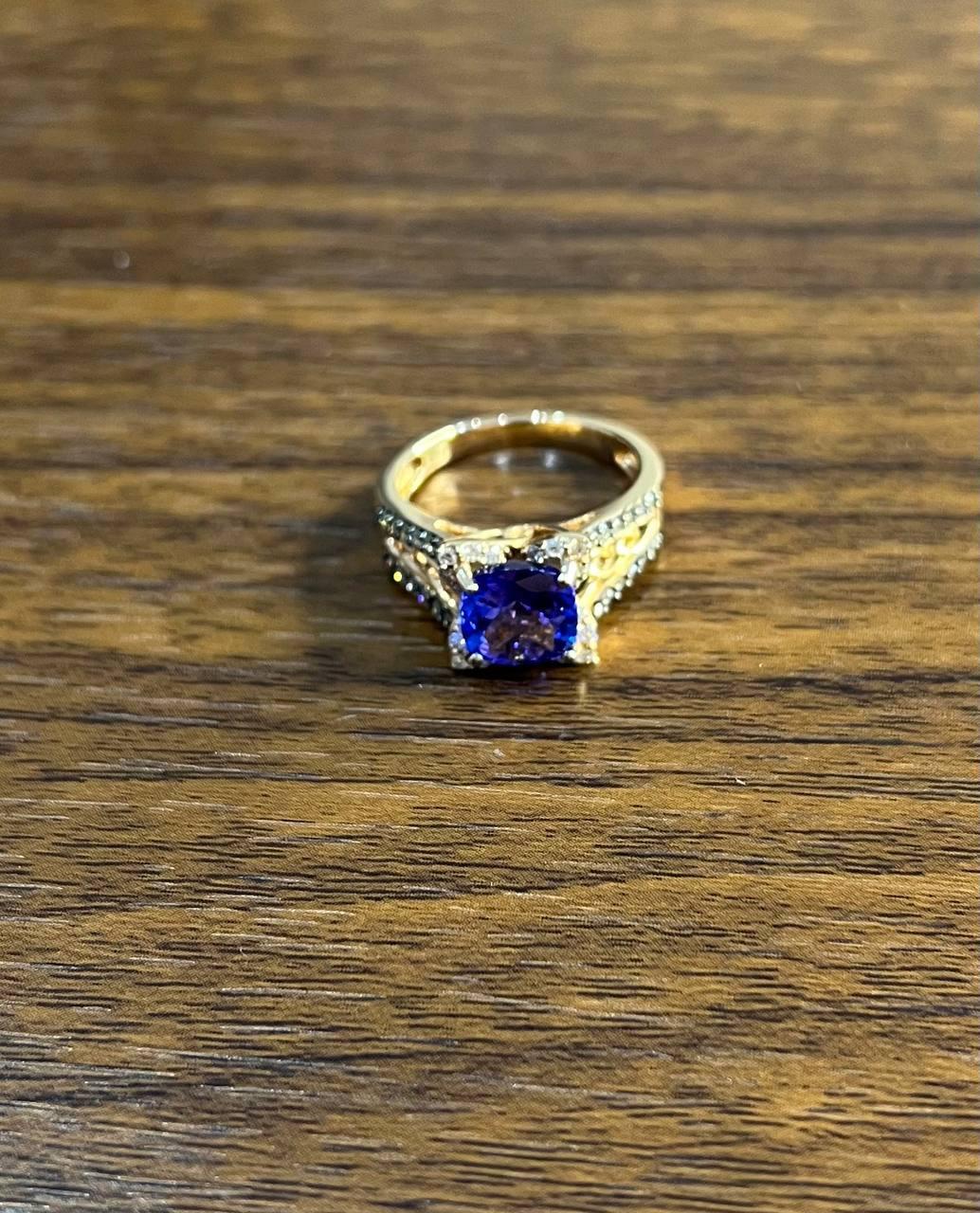 A symphony of elegance and brilliance.

This striking statement ring features a captivating deep blue center tanzanite, expertly set to draw the eye. The round cut gem is flanked by intricate detailing, with shimmering accent diamonds that enhance