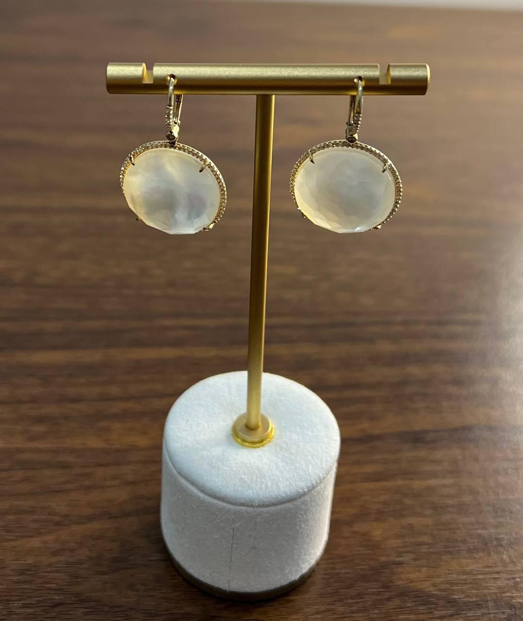 Estos elegantes pendientes están fabricados en oro amarillo de 14 quilates. Presentan piedras redondas de nácar blanco, acentuadas por diamantes con un peso total en quilates de 0,57.  El diámetro mide 20 mm de longitud.