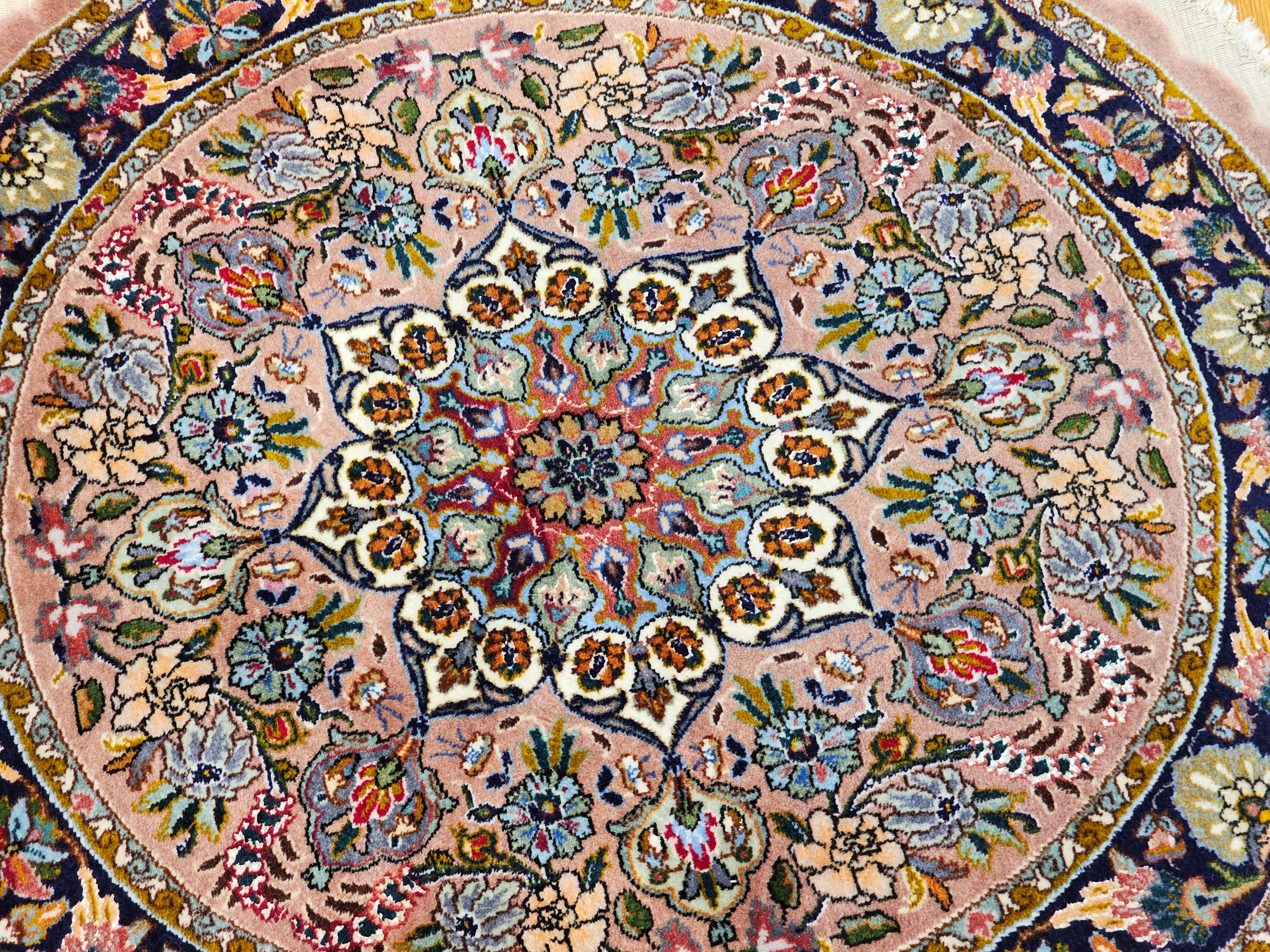 A beautiful and rare round shaped Persian Tabriz area rug in floral pattern from the 4th quarter of the 1900s .   The field is pale pink with flowers and branches in pink, baby blue, green, brown, red, and cream.  The border is navy blue with