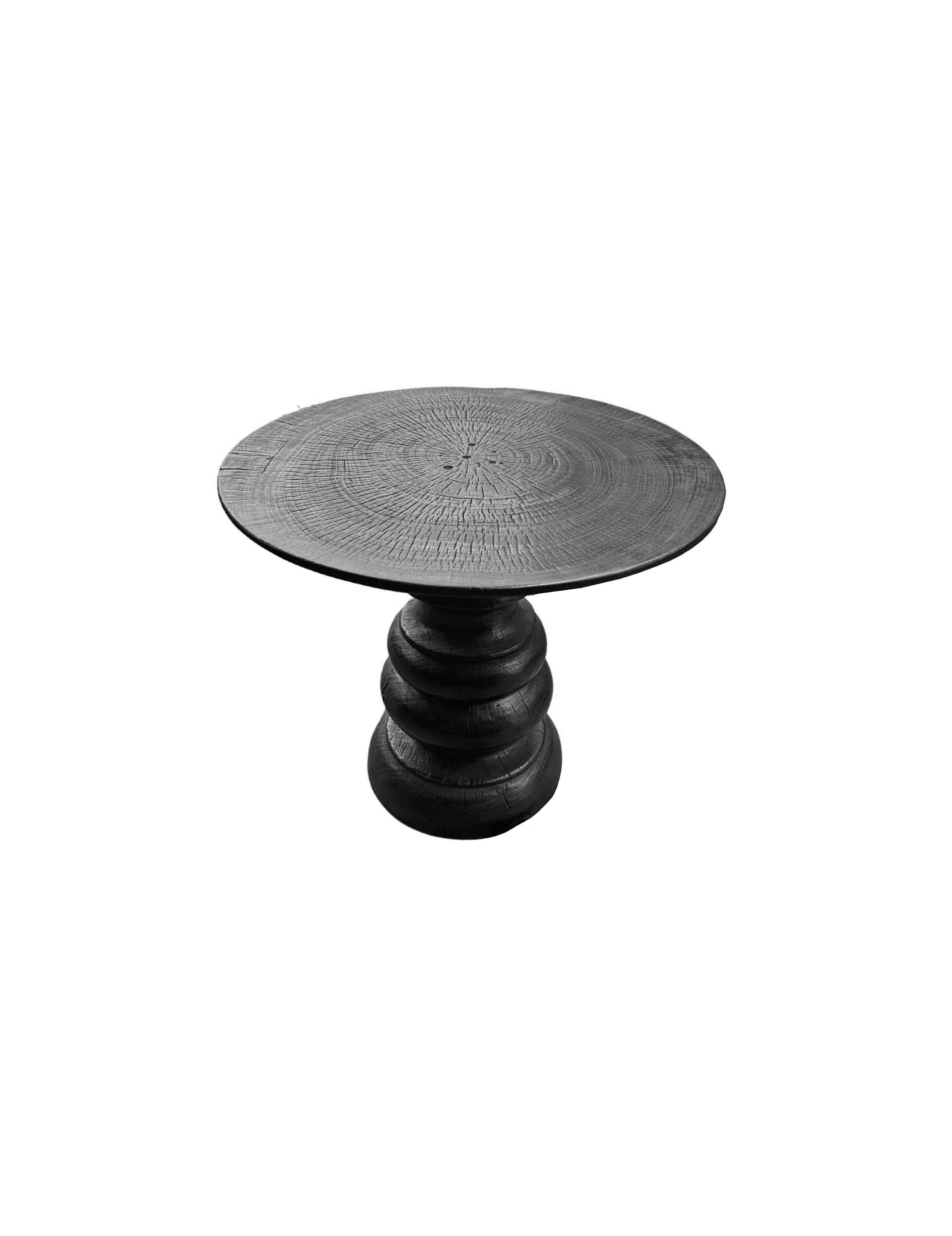 A wonderfully organic round side table. Its rich black pigment was achieved through burning the wood three times. Its neutral pigment and subtle wood texture makes it perfect for any space. A uniquely sculptural and versatile piece, featuring carved
