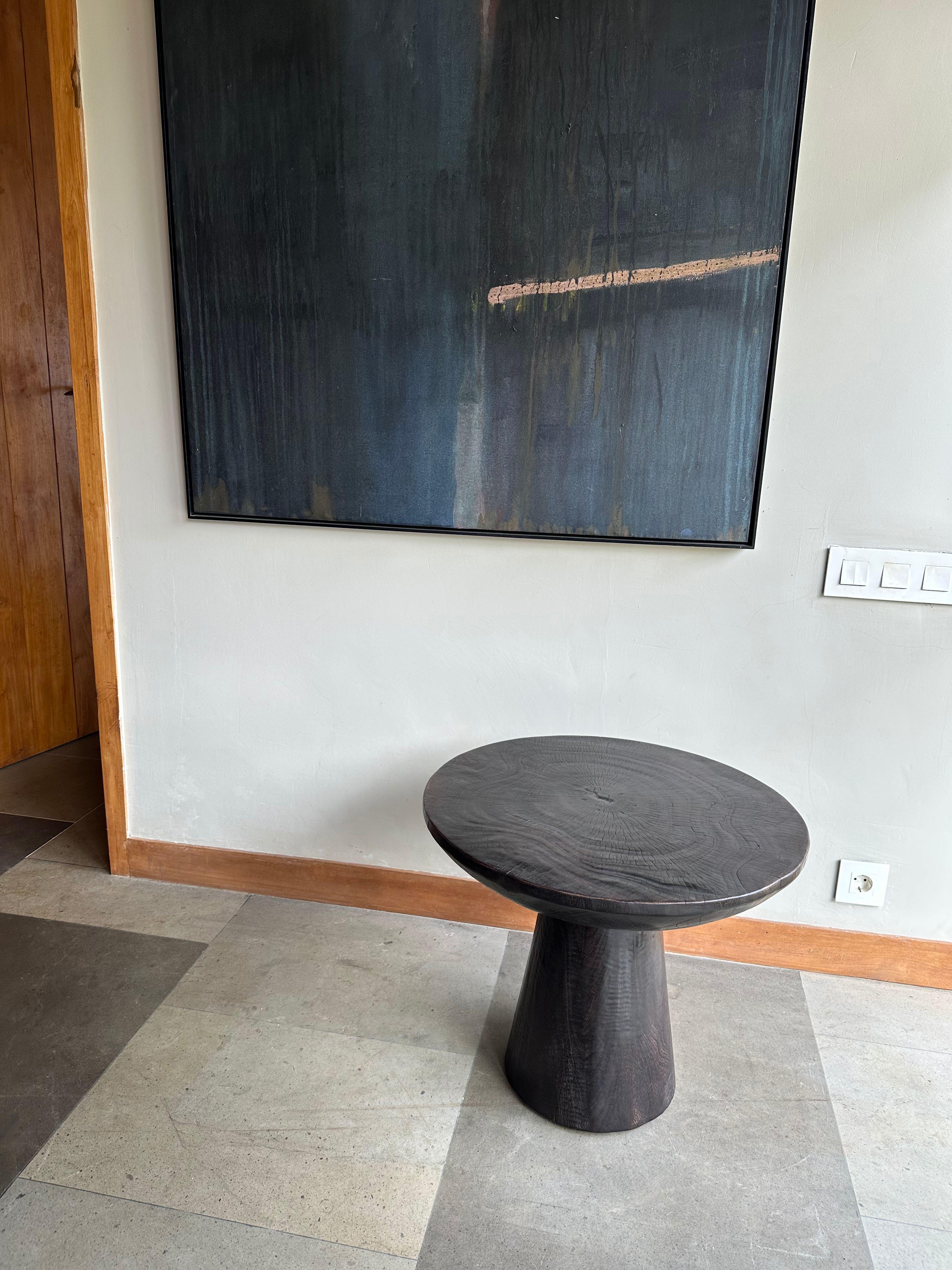 A wonderfully organic round side table. Its pigment was achieved through burning the wood multiple times and finished with a clear coat. Its neutral pigment and subtle wood texture makes it perfect for any space. This table was crafted from mango