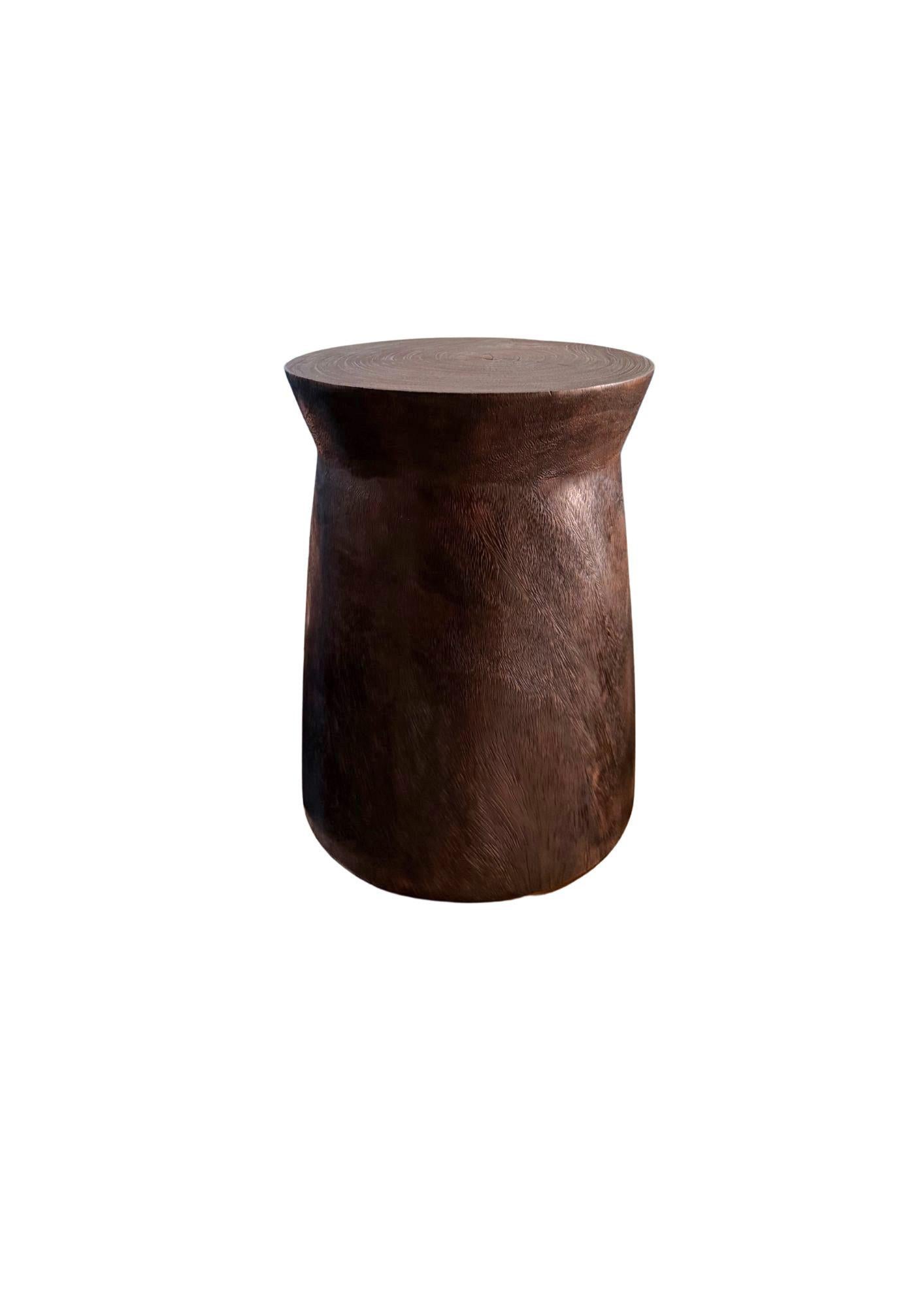 Eleva tu espacio con esta impresionante mesa auxiliar, meticulosamente elaborada a mano a partir de una única pieza de madera maciza de Suar. Con un rico acabado marrón oscuro espresso, esta pieza se ha quemado expertamente varias veces para