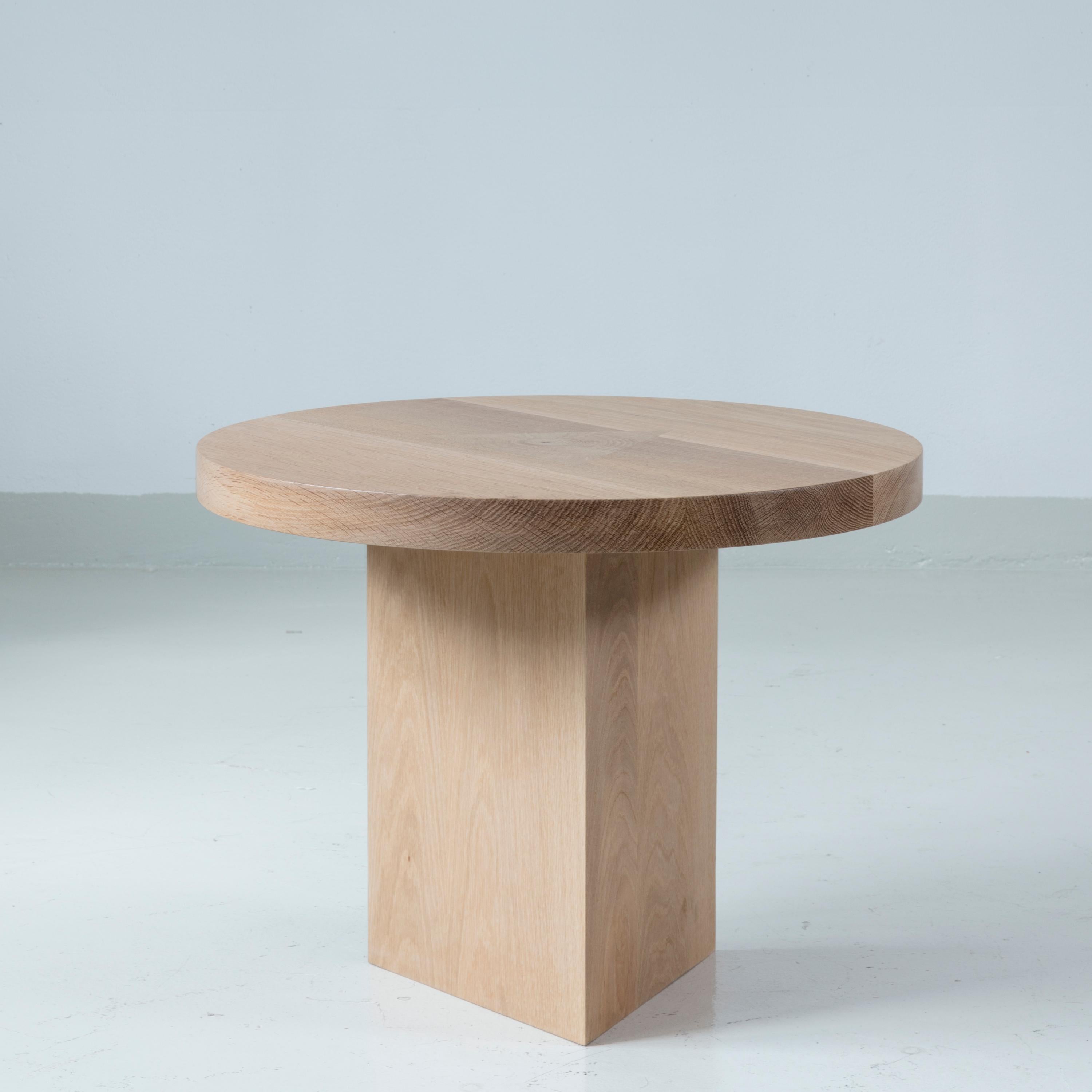 Circular side table in oak with triangular leg that cuts through the round top. Perfect proportions, warm and sober.