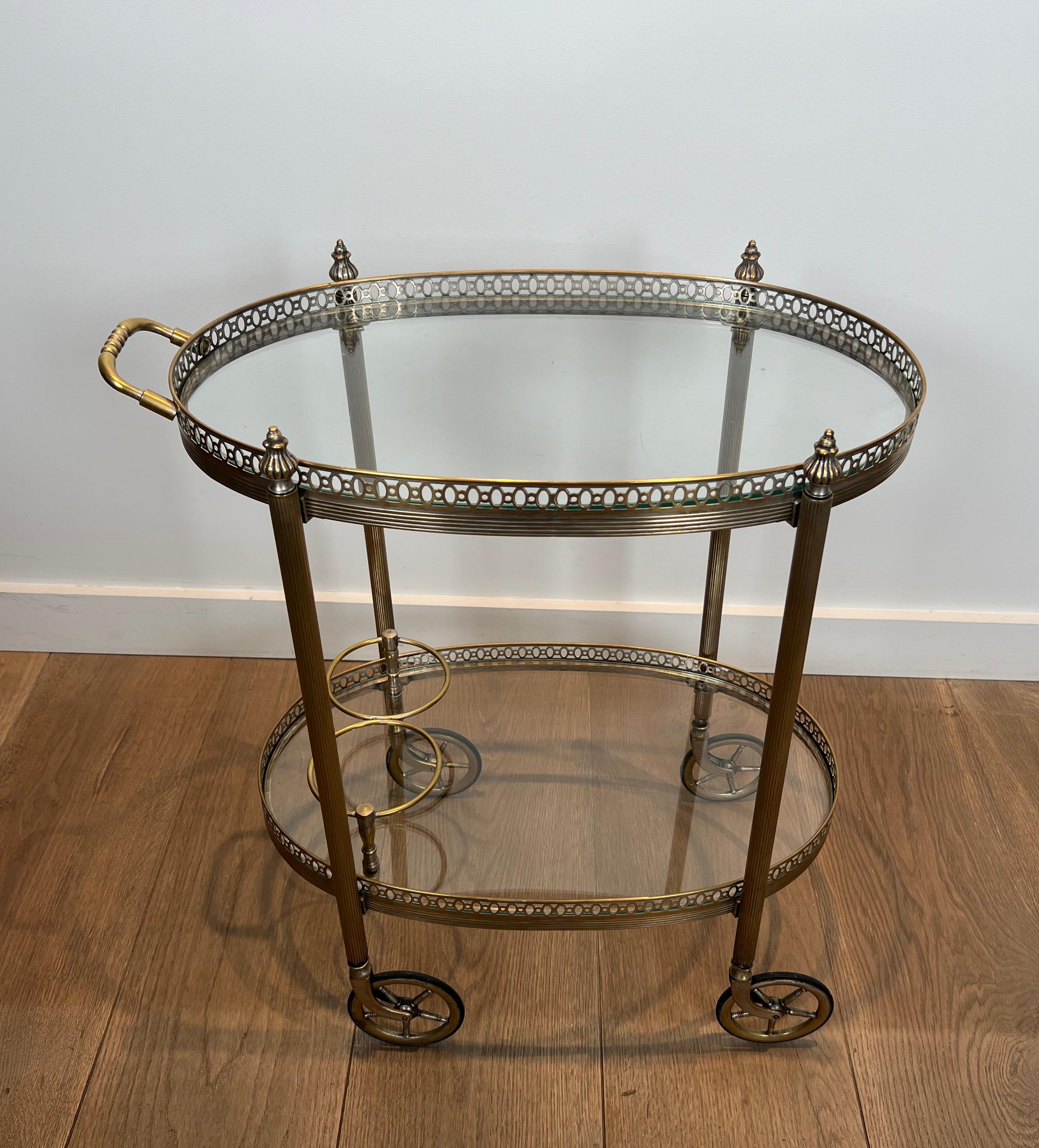 This fine and elegant neoclassical style oval bar cart is made of silvered brass with two trays and a bottle holder. This is a French work by Maison Bagués. Circa 1940