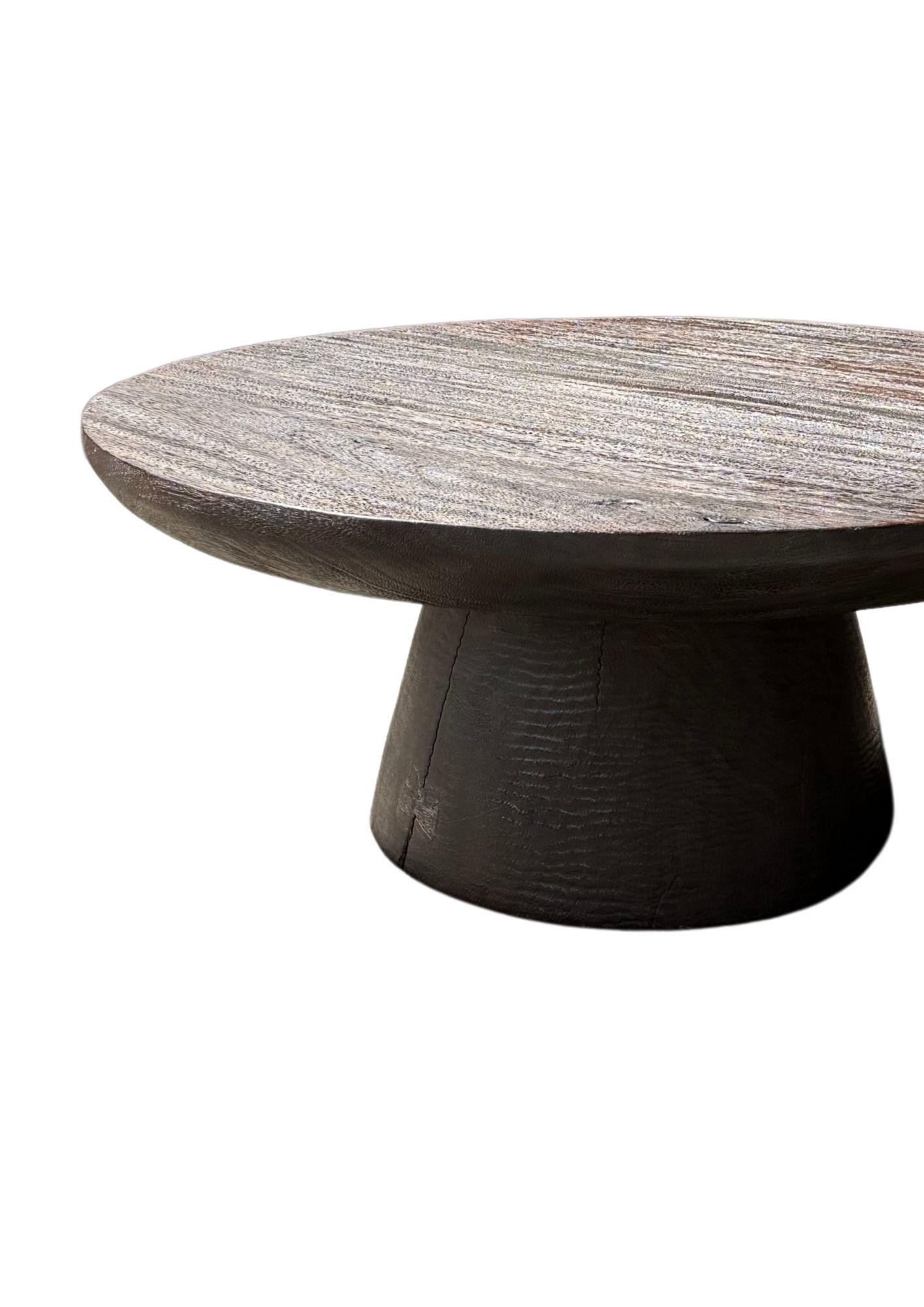 Wir stellen Ihnen unseren exquisiten runden Sofatisch aus Suar-Holz vor, der mit einer markanten gebrannten Oberfläche versehen ist, die die natürliche Schönheit des Holzes hervorhebt. Dieses atemberaubende Stück zeigt eine reiche Palette an