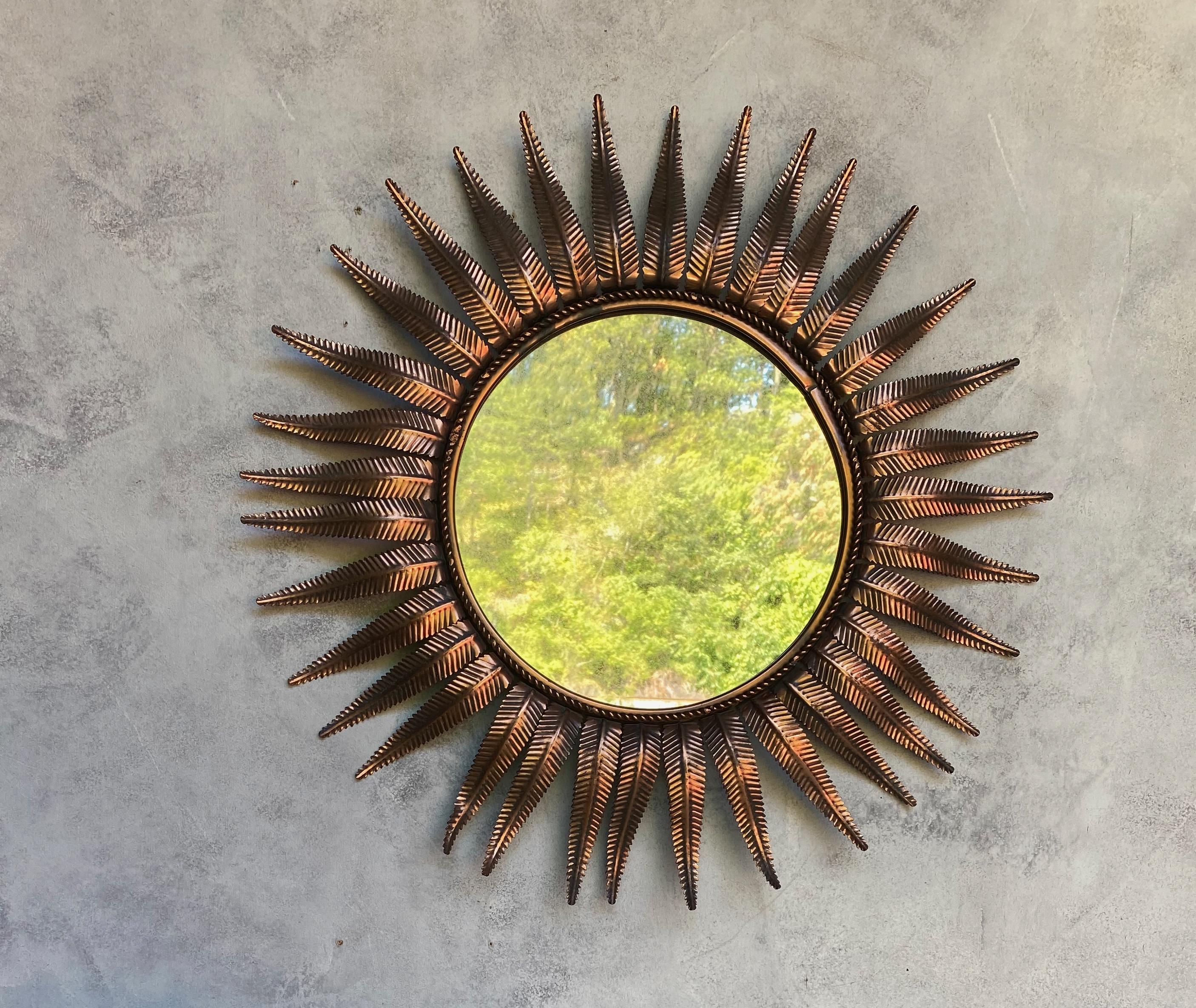 An elegant Spanish copper-plated sunburst mirror made in Spain in the 1950s. This Mid-Century Modern piece boasts a stunning copper-plated metal frame of stylized fern leaves in a sunburst pattern. The mirror's original richly patinated copper