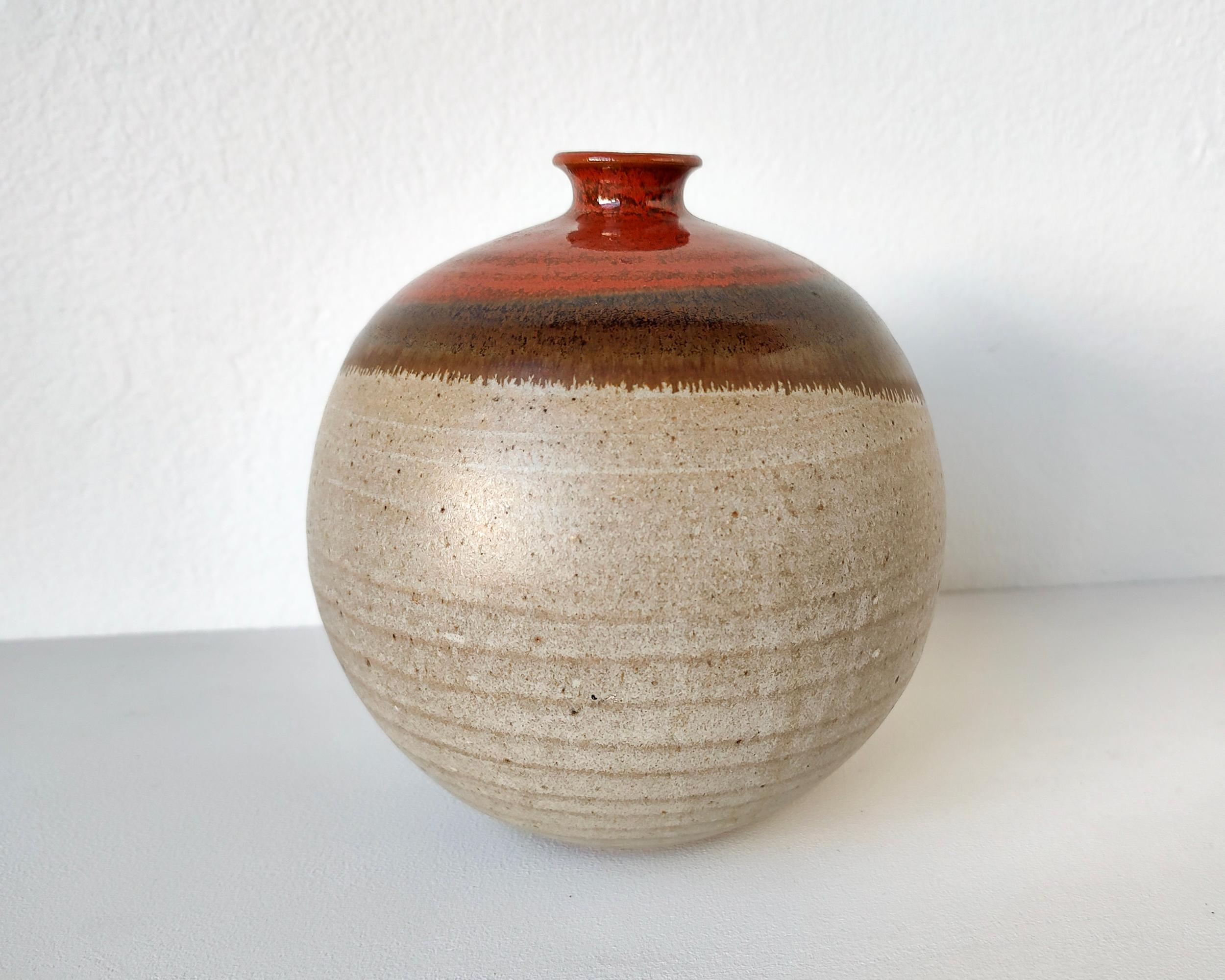 Wheel thrown stoneware orb-shaped vase with a narrow neck. Studio ceramic vessel made beautifully with visible throwlines and a hidden foot. Red iron glaze over a matte white glaze are layered to create an overlapping glaze design.