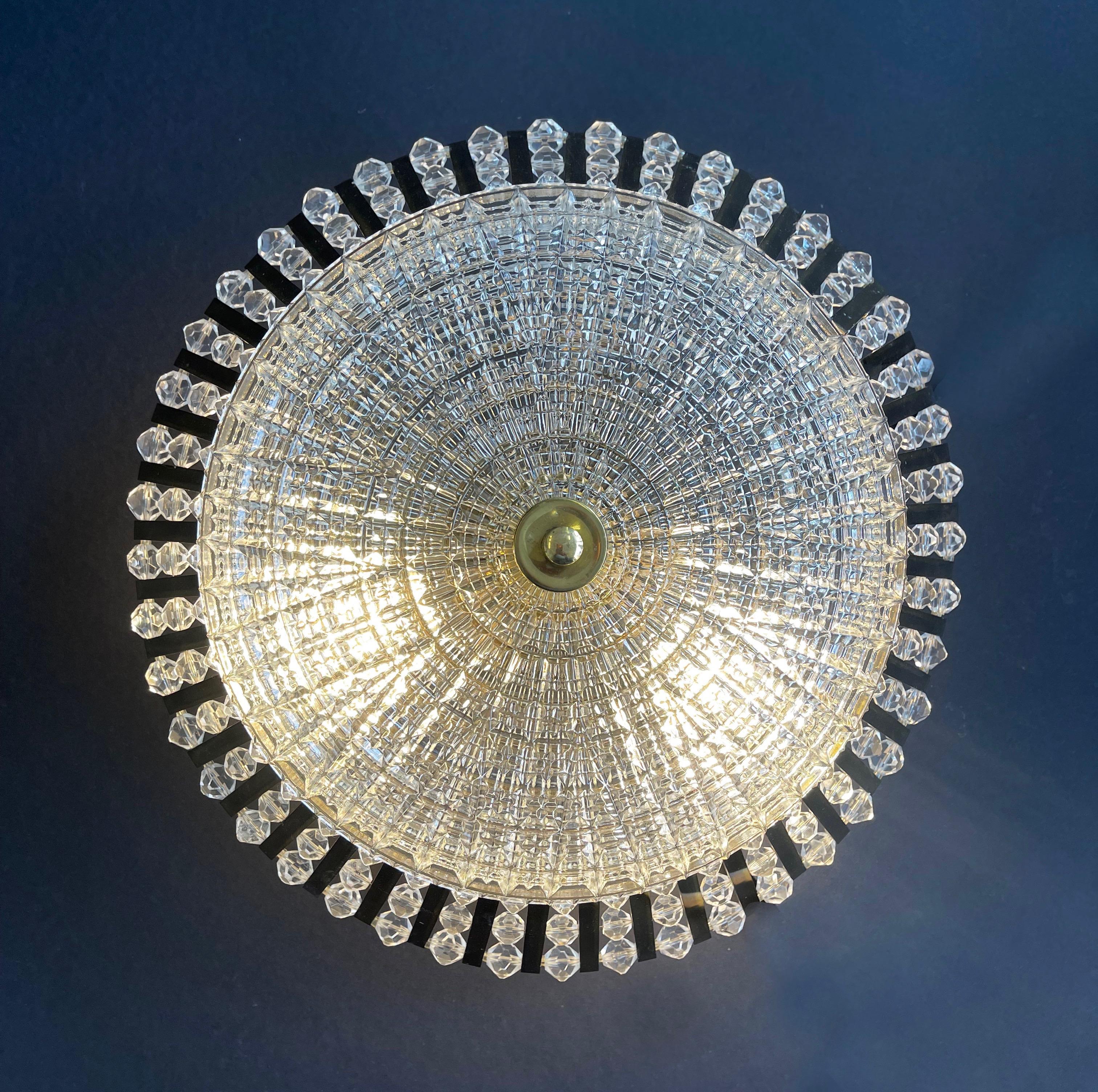 Splendida e lussuosa plafoniera nello stile di Emil Stejnar, Austria.
Il disco in cristallo degli anni '70 è coronato da una corona di ''raggi'' in ottone collegati da 3 file di perline acriliche.
Leggermente sospesa dal soffitto, la lampada offre
