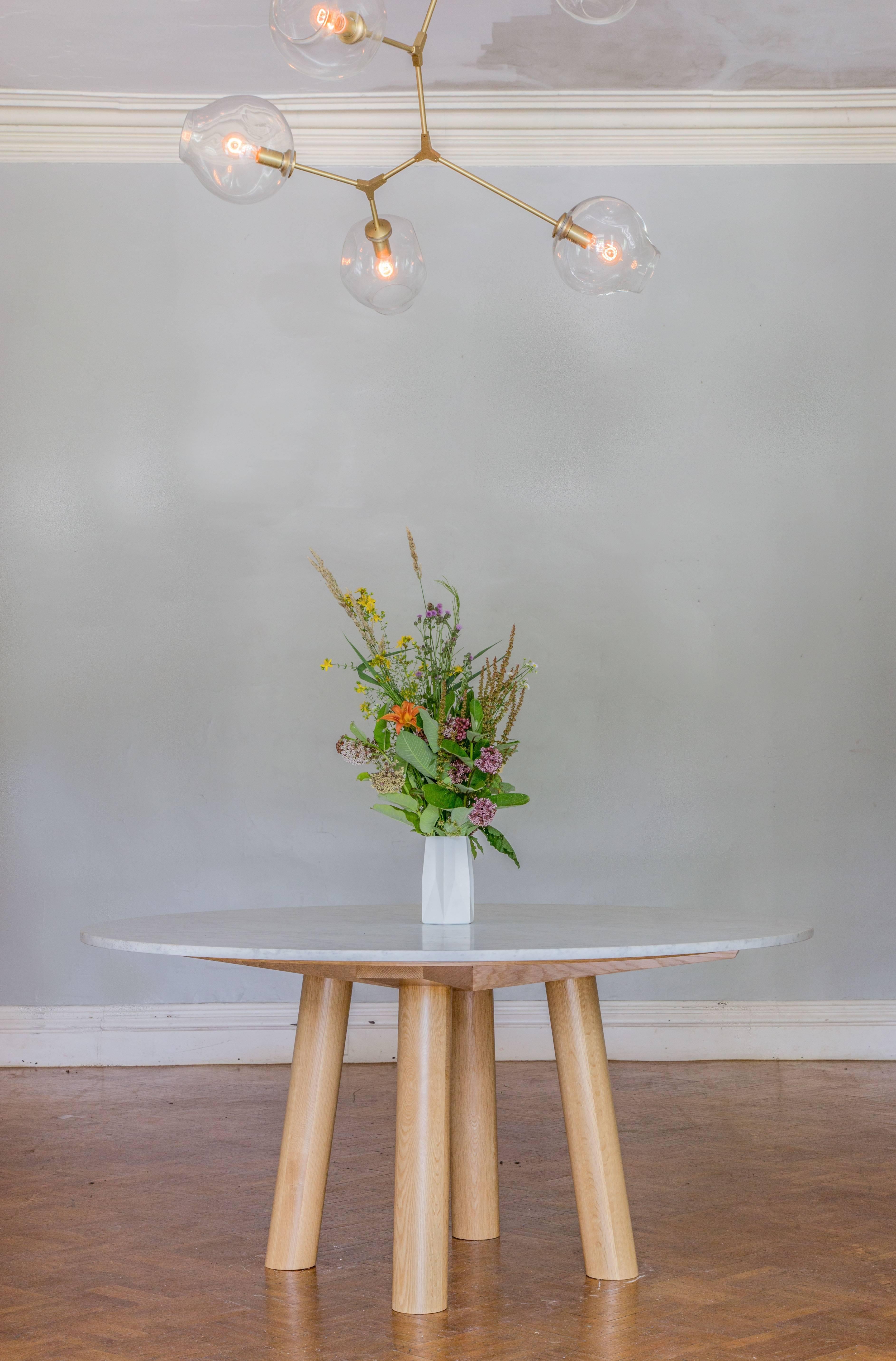 Dieser moderne, minimalistische Esstisch verfügt über runde Beine mit großem Durchmesser und kühne Gestellstützen, auf denen eine Platte aus Stein oder Hartholz ruht. Die Tischplatte weist ein Holzoberflächendetail auf, das die Platte zum Sockel