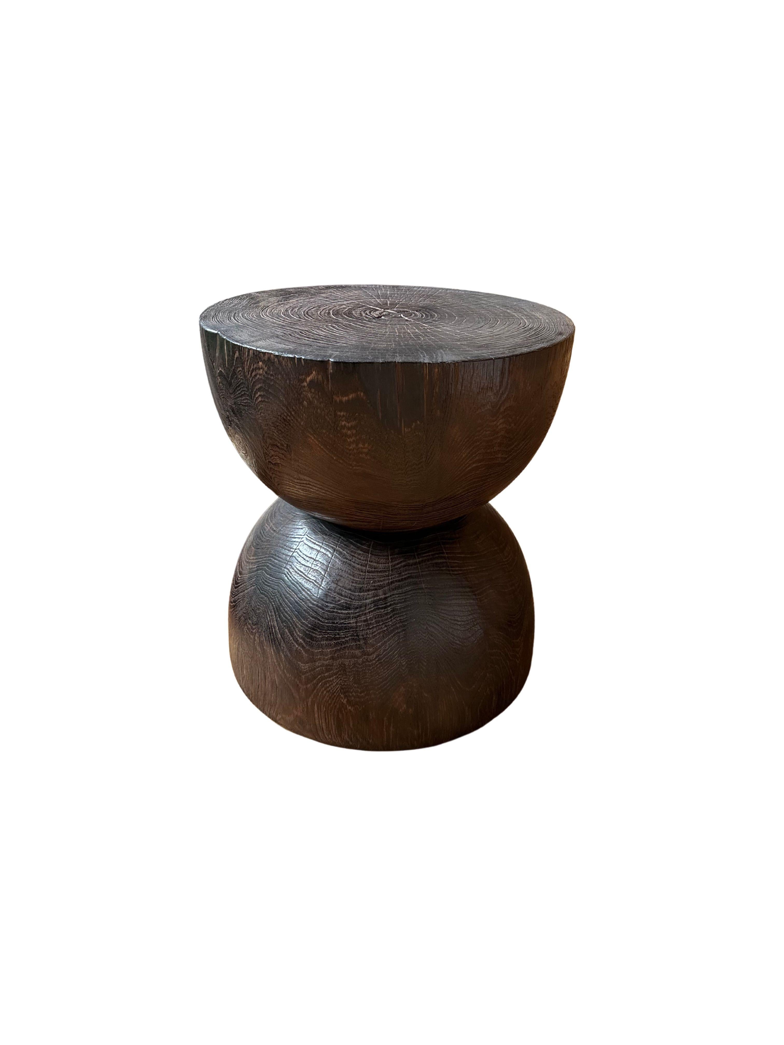 A wonderfully sculpted side table, crafted from a single block of teak wood. It features wonderful wood textures as well as an hour glass form. To achieve its pigment the wood was burnt several times and finished with a clear coat. 