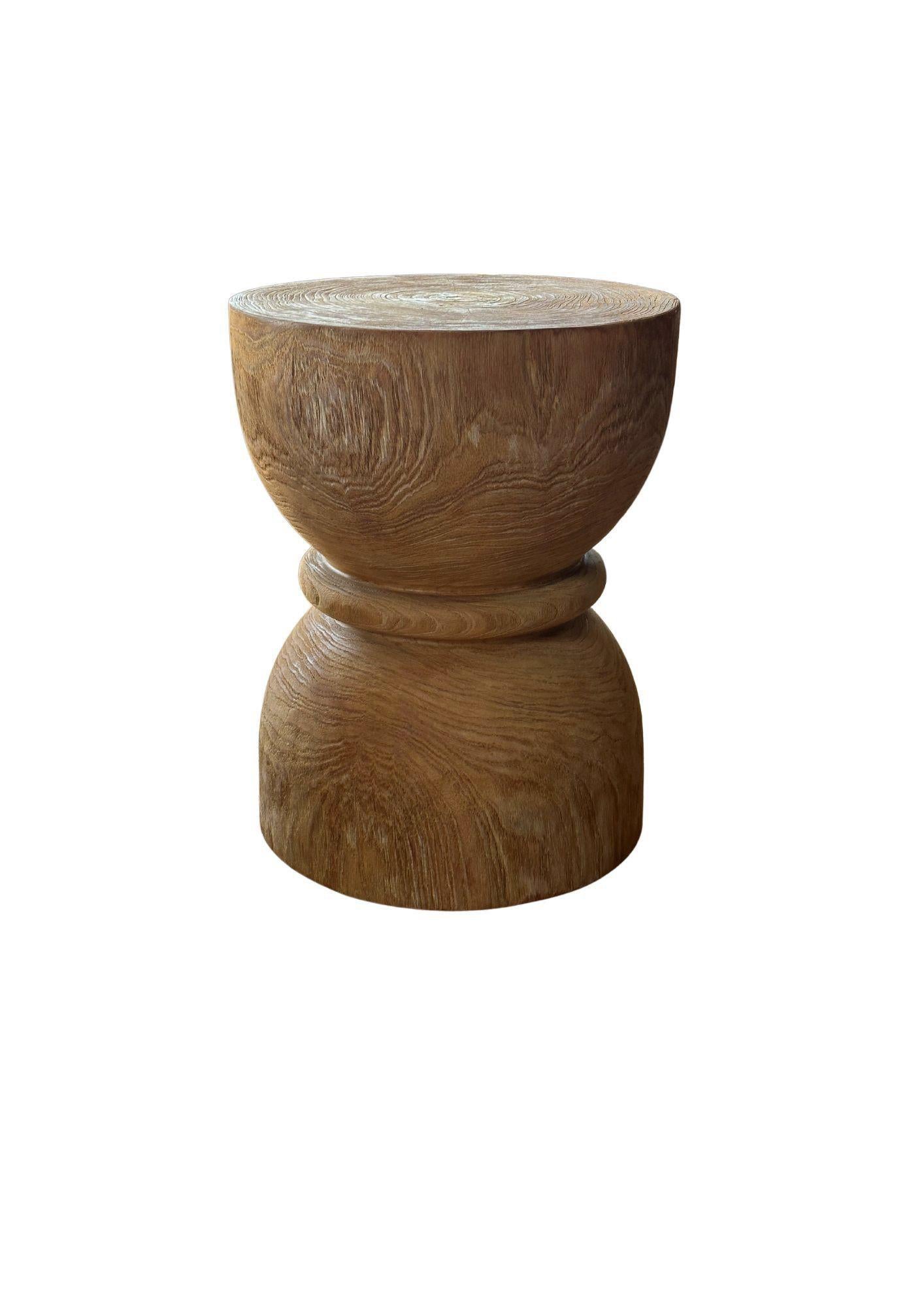 Une table d'appoint merveilleusement sculptée, fabriquée à partir d'un seul bloc de bois de teck. Il présente de merveilleuses textures de bois ainsi qu'une forme de sablier. Il présente une finition naturelle, poncée à plusieurs reprises, puis