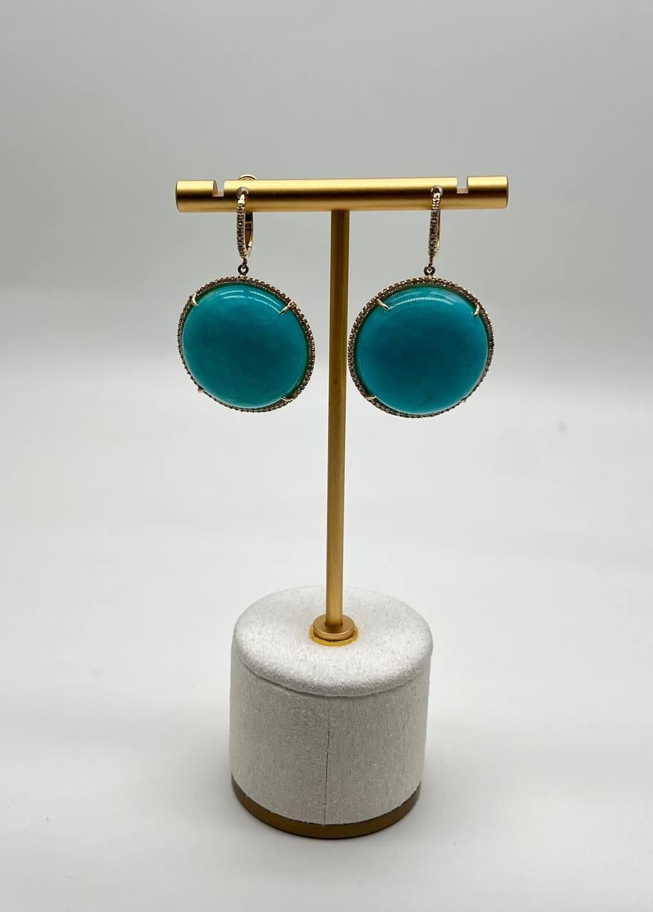 These striking earrings are crafted in 14k gold. Each earring features a large, round turquoise stone, framed with delicate detailing. 0.33 CTW Diamonds. 20 x 15 mm Turquoise size proportions.