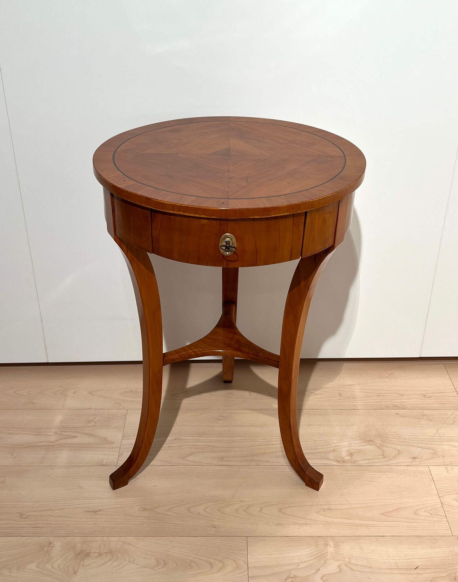 Round three-legged Biedermeier side table, Walnut, South Germany circa 1820.
 
Walnut veneered and solid. Restored and hand polished with shellac. 
Top book-matched veneered with surrounding ebony inlay band. Front centre drawer, lockable.