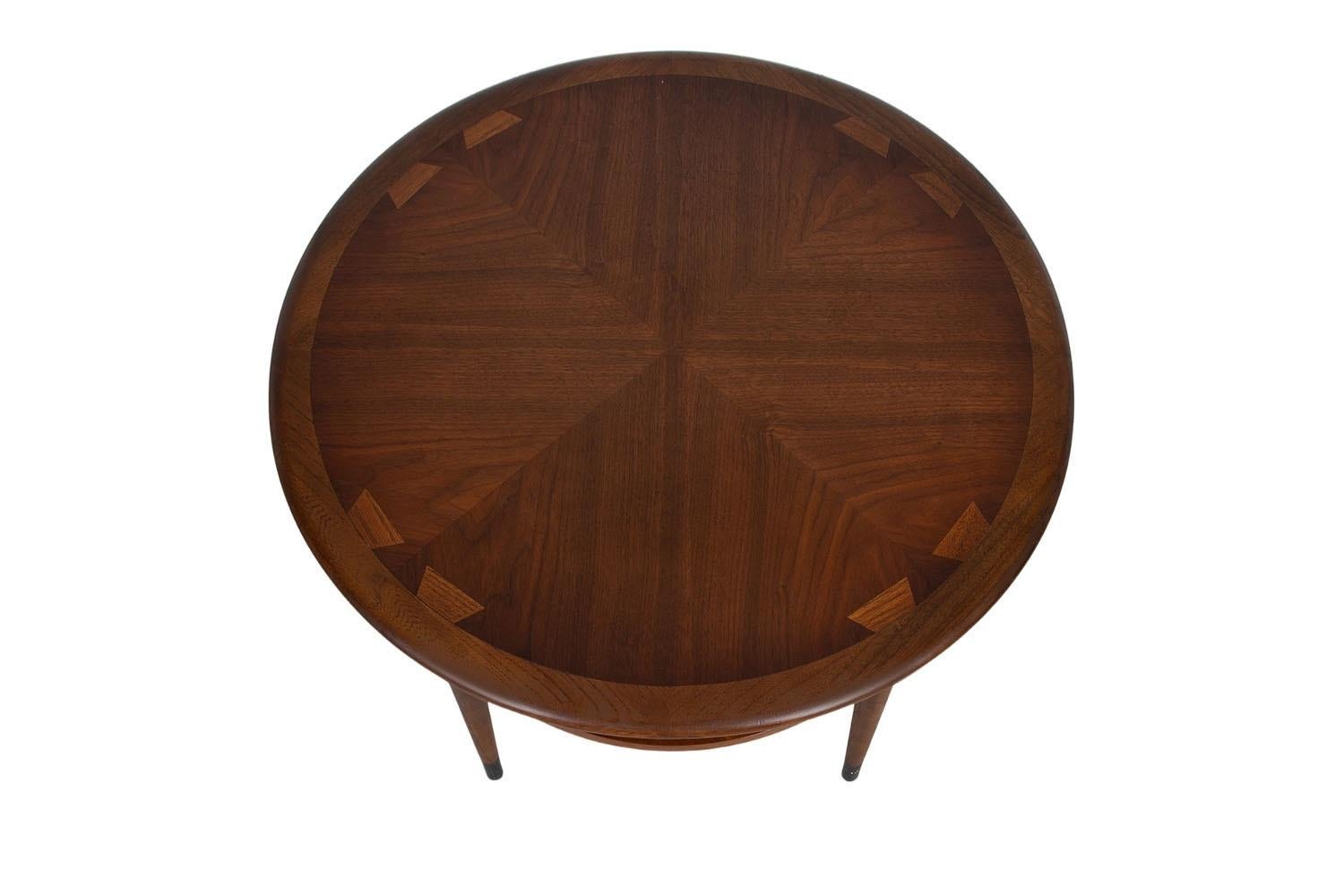 A beautiful round tiered end table by Andre Bus for Lane Furniture Co. from the Lane ‘Acclaim’ collection. Remains in good condition throughout. Featuring stunning, signature dovetailed design, in a vivid contrast against the surface with walnut top