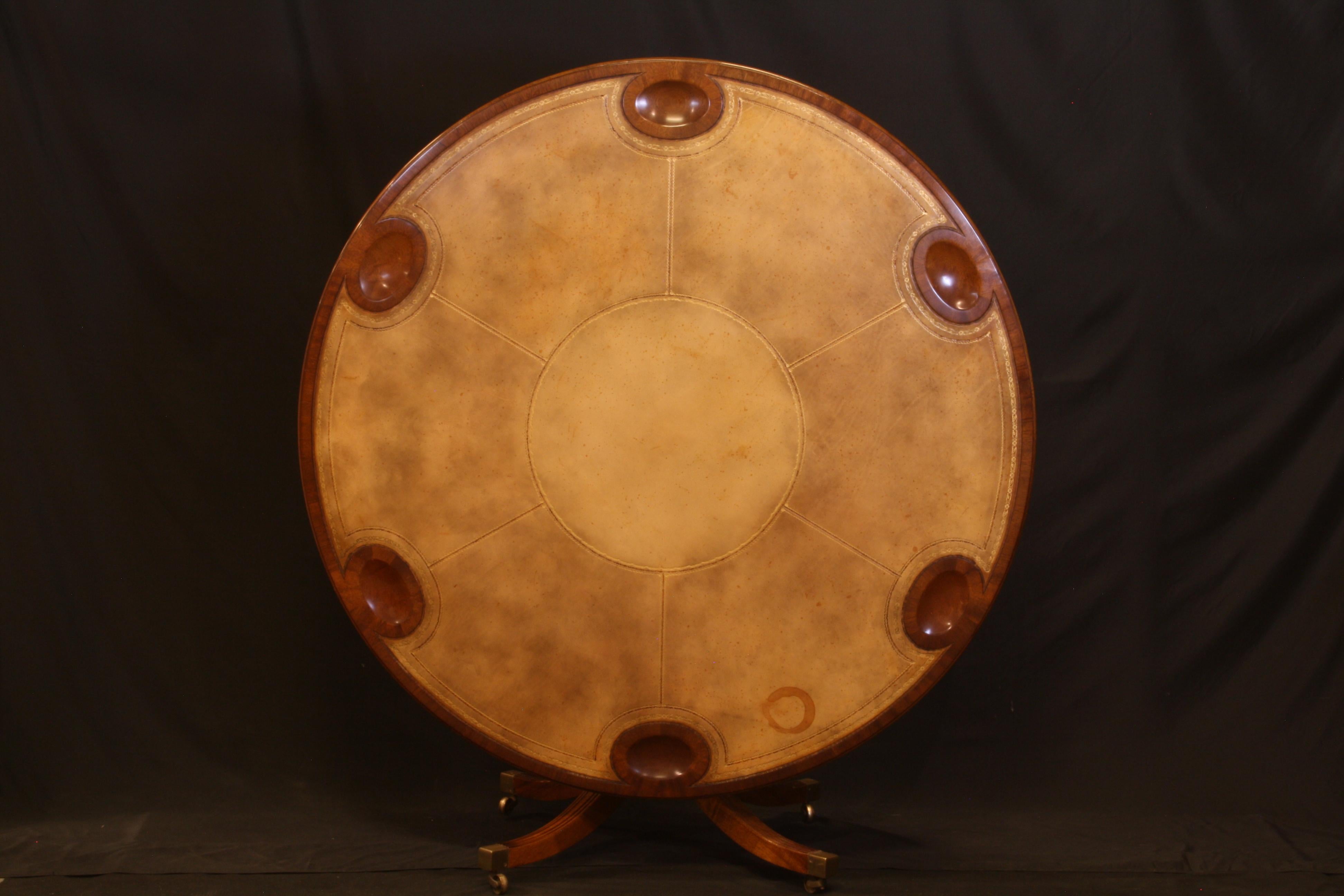Round leather top games table, by William Tillman. A very unique, English made, circa 1975, traditional English tilt top table with mahogany pockets for gaming pieces.
The top is mahogany with hand embossed, gold accented leather with a rich mellow