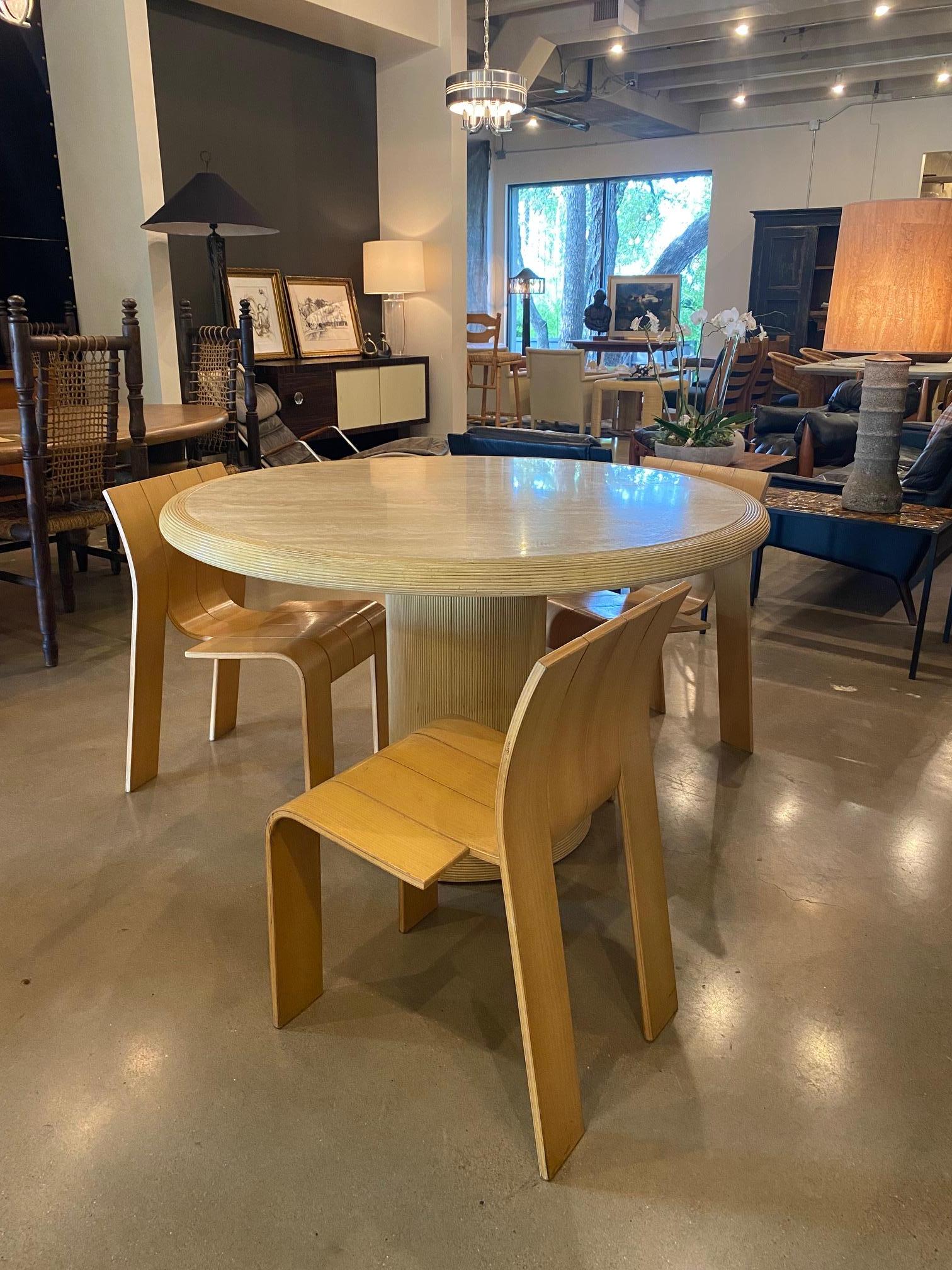 Tavolo da pranzo rotondo con base a piedistallo in travertino e rattan.  Il rattan a coste chiare avvolge la base del piedistallo e il bordo arrotolato del piano in travertino massiccio.  È disponibile anche un tavolo da cocktail coordinato. 
