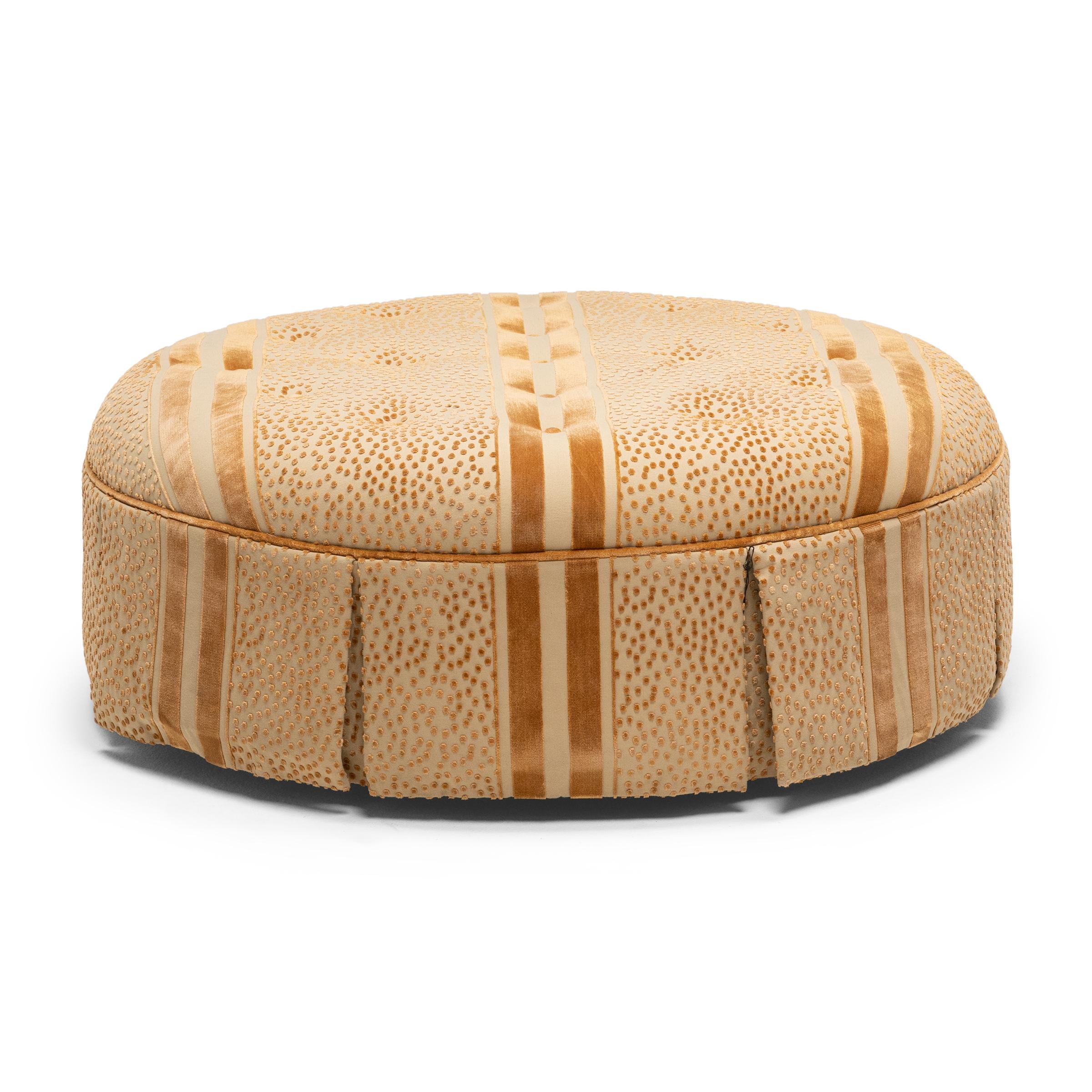This large round ottoman is enveloped in opulent cut velvet upholstery embellished with a dotted pattern reminiscent of leopard print and bold lines that flow seamlessly across the top and sides. The cushioned top has a tufted design held in place