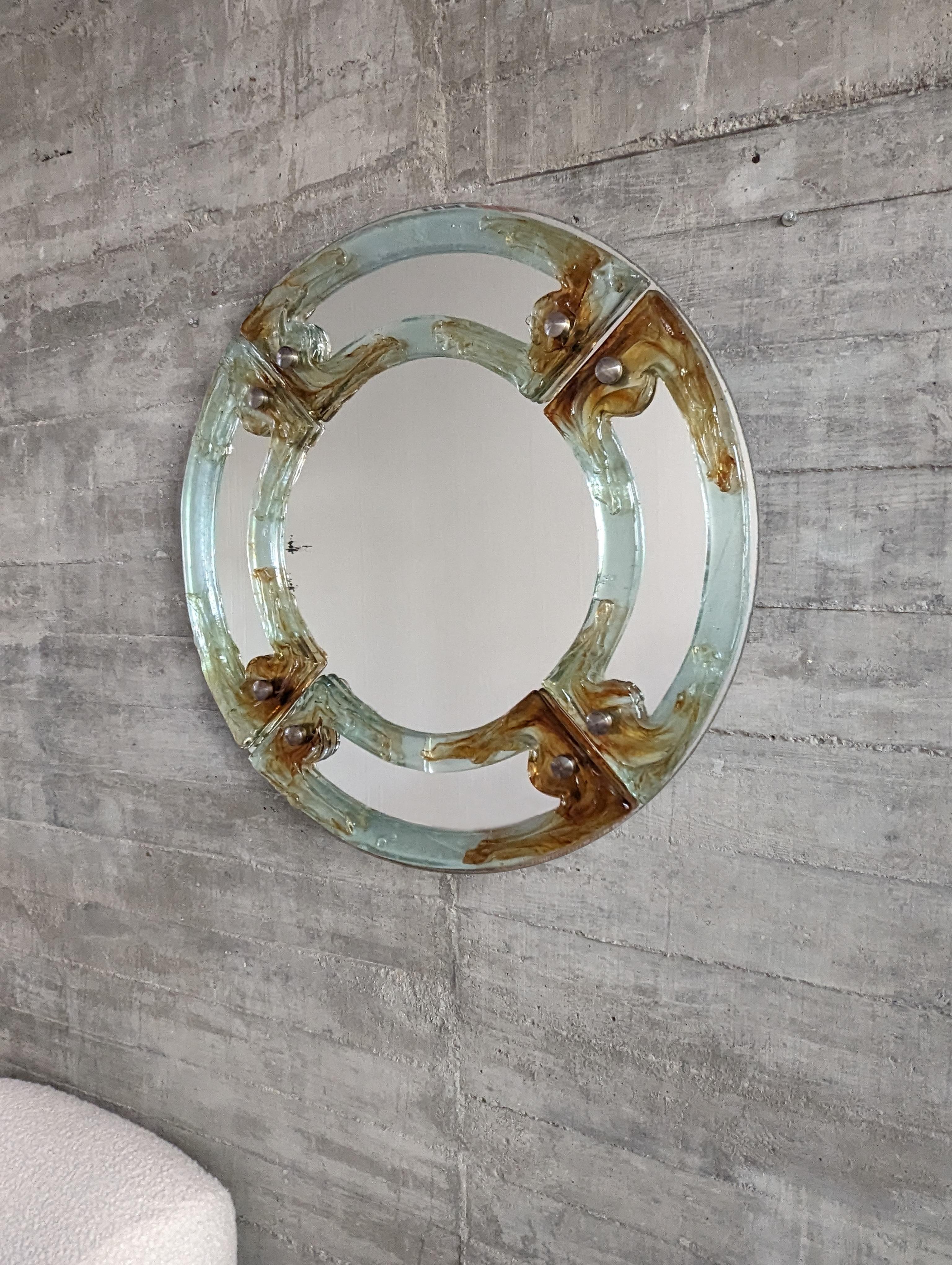 Spectacular round Murano glass mirror in amber tones is an authentic treasure from the 1960s. Its exquisite Murano glass reflects the rich artisanal heritage of Venice, with a design that captures the essence of the golden age of Italian