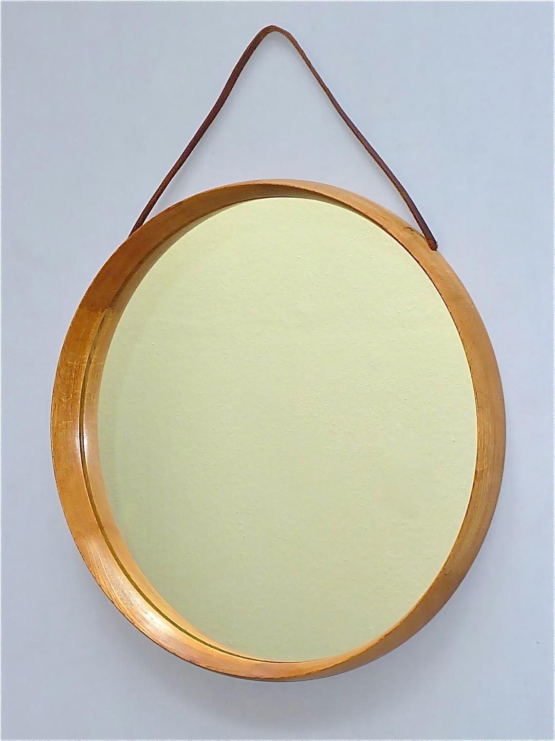 Miroir mural rond en bois de chêne suédois avec sangle en cuir, conçu par les célèbres Uno & Osten Kristiansson et produit par Luxus à Vittsjö, Suède, dans les années 1960. Le miroir moderne Scandinavian fait à la main a une largeur de 45 cm / 17.72