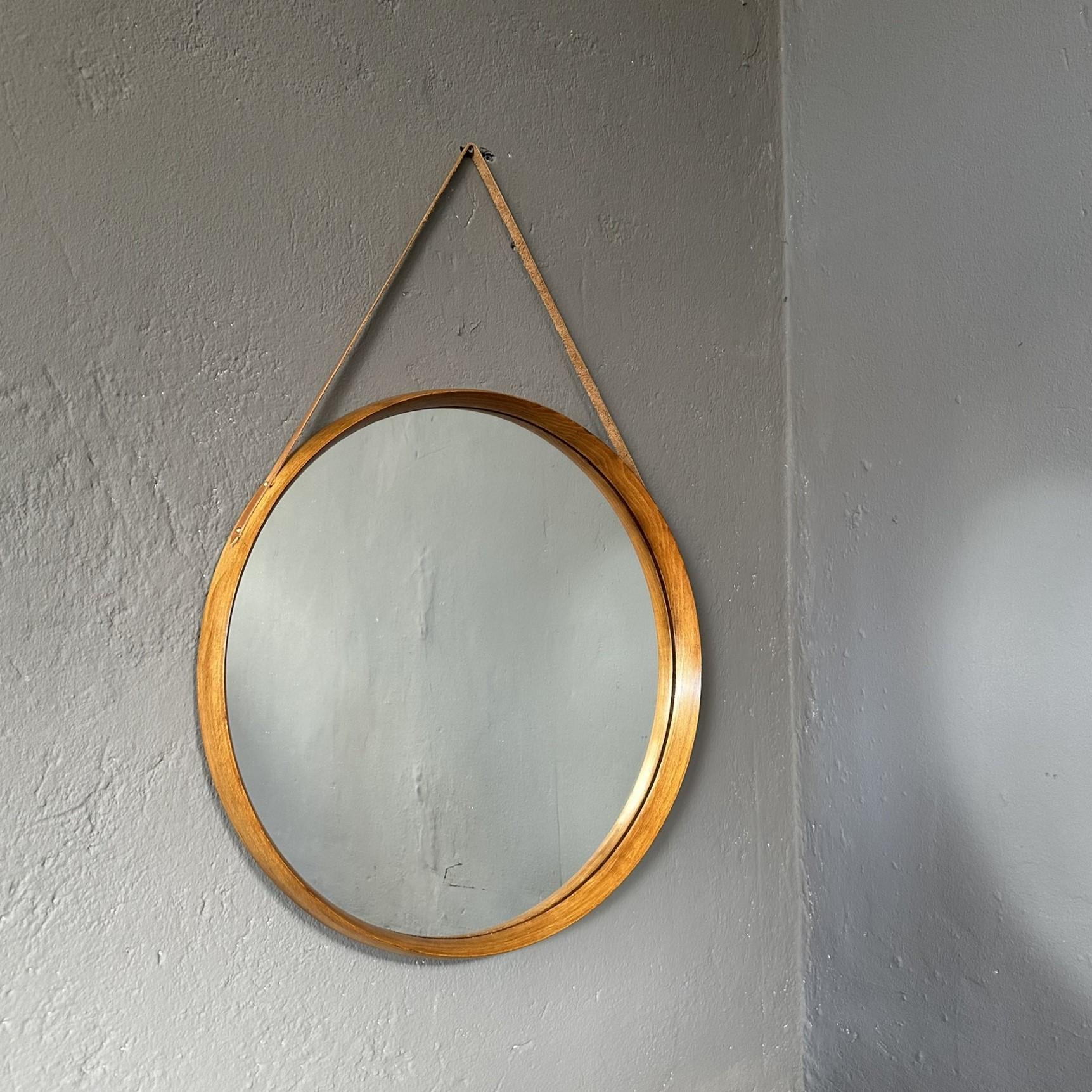 Specchio da parete rotondo degli anni '60, di manifattura italiana.
Lo specchio ha un diametro di 51 cm e una cornice in teak marrone chiaro.
Per appenderlo alla parete è dotato di un cinturino in pelle.
C'è una piccola macchia sulla superficie