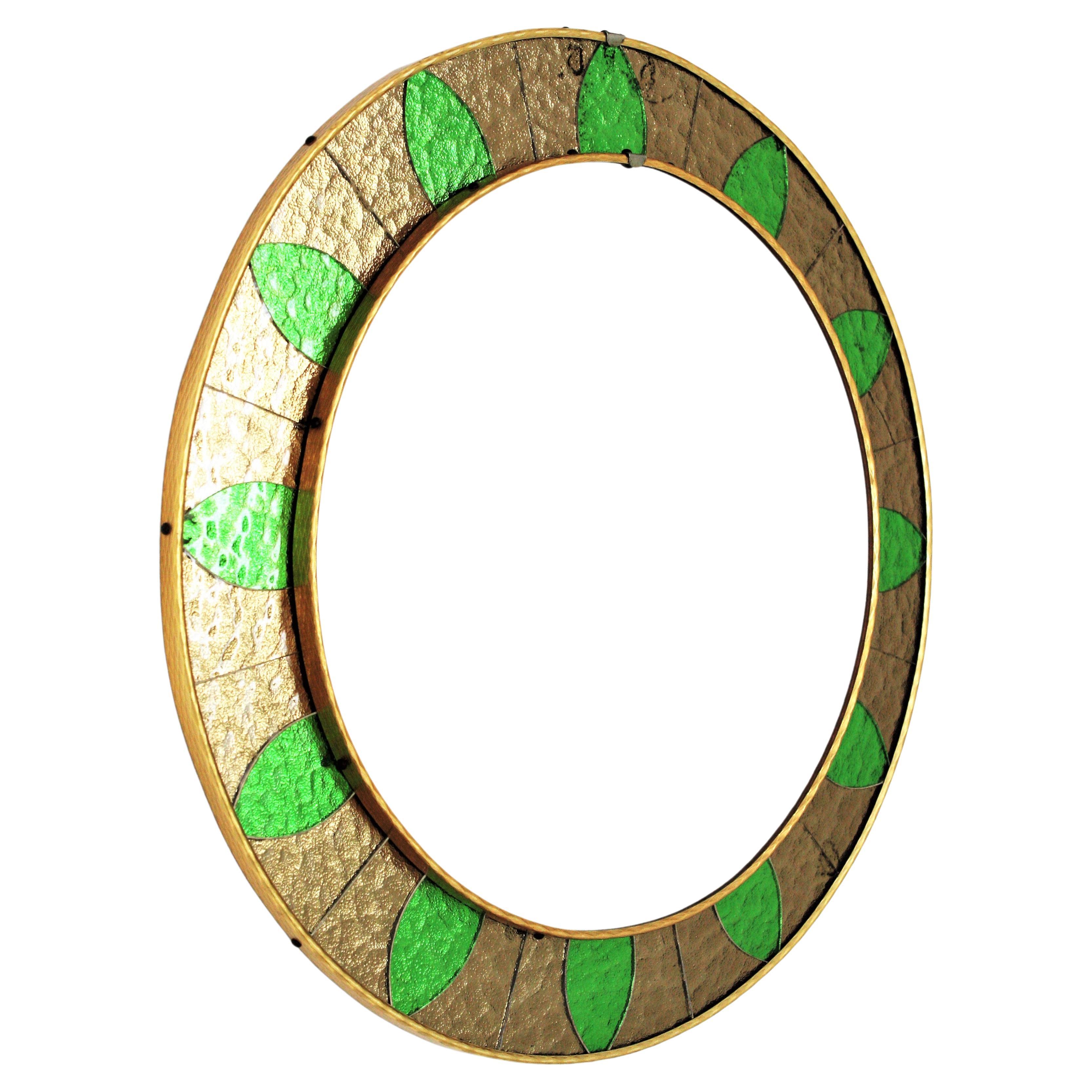 An stylish Mid-Century Modern round mirror with green and bronze color glass frame. Spain, circa 1960s.
The frame is comprised by a background made of iridiscent glass mirrored pieces accended by green glasses in sunburst disposition.
The glass