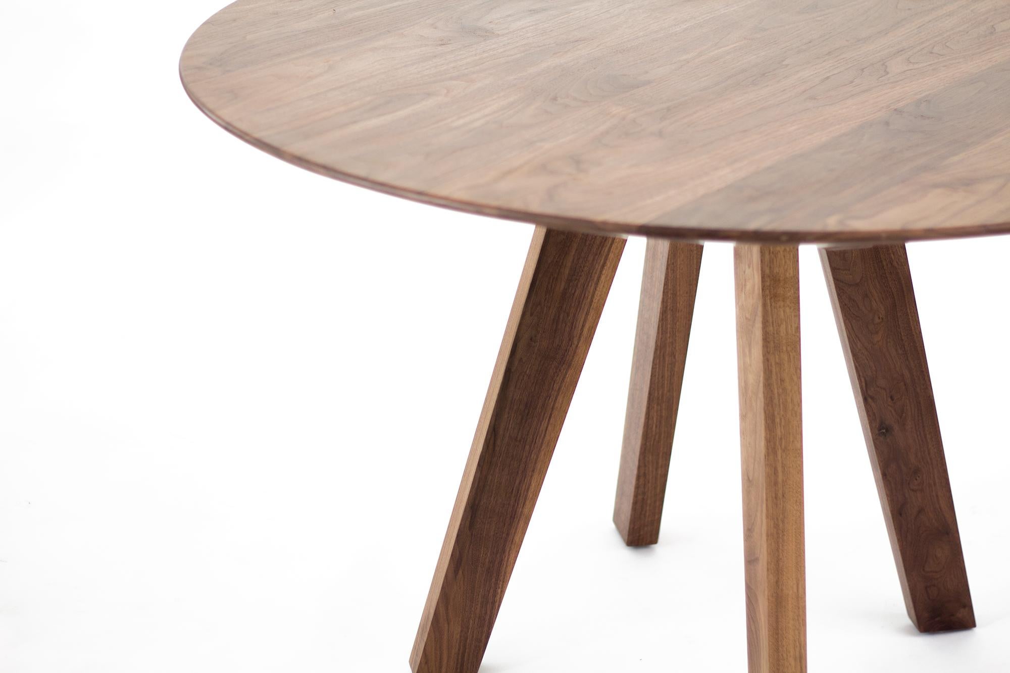 This round dining table is crafted entirely from rich, solid walnut, highlighting the natural beauty and warmth of the wood. Its design features four sturdy, well-crafted legs that provide excellent stability while maintaining a sleek and modern